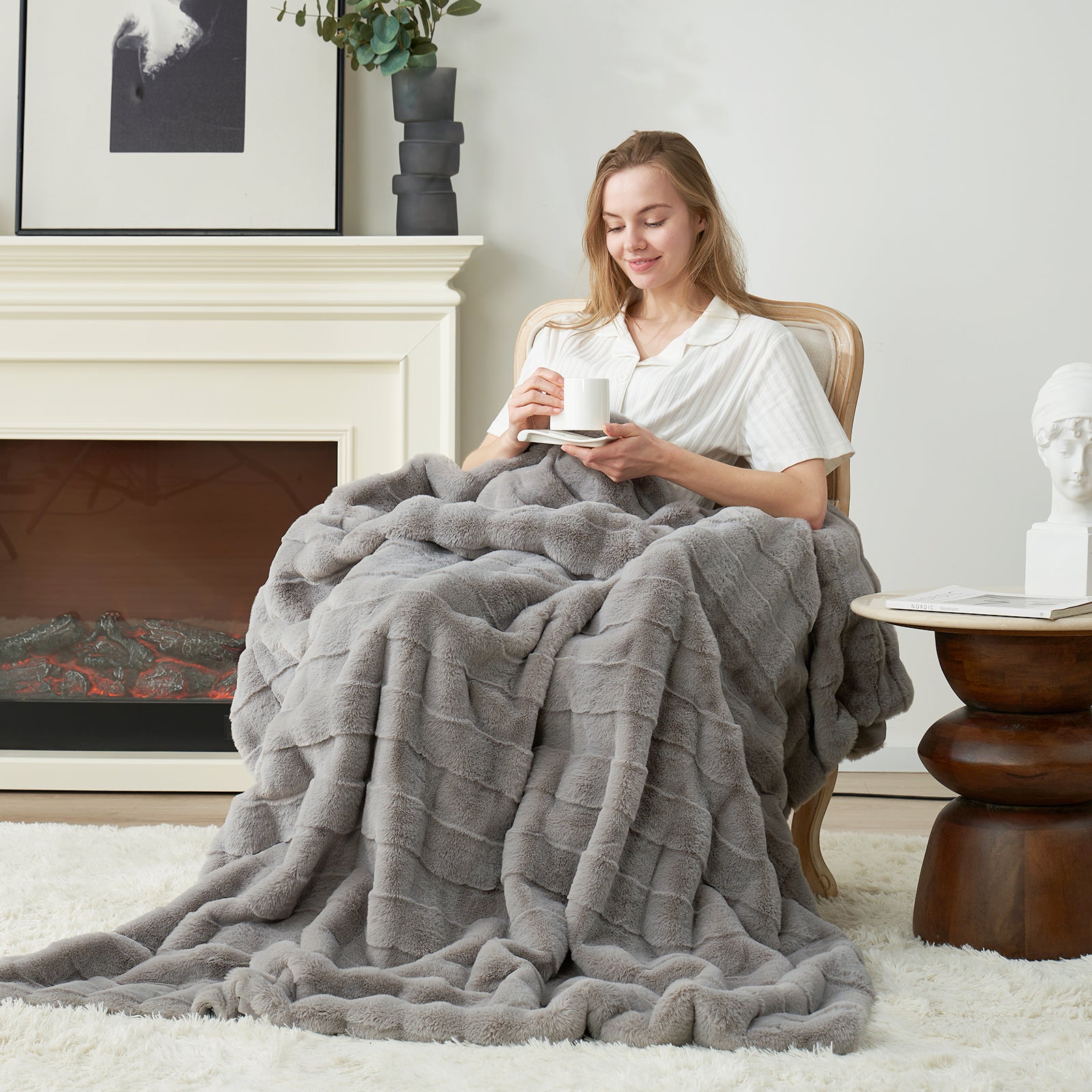 Cozy Bliss gray faux fur throw blanket draped over a woman sitting in a chair, holding a cup, promoting comfort #color_Grey