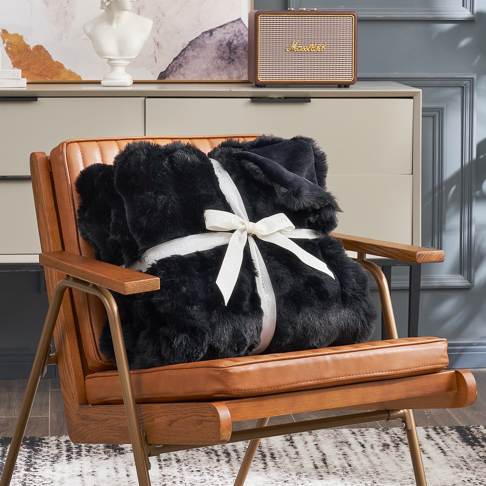 Cozy Bliss black faux fur throw blanket, tied with ribbon, on a brown leather chair. Soft and cozy blanket #color_Black