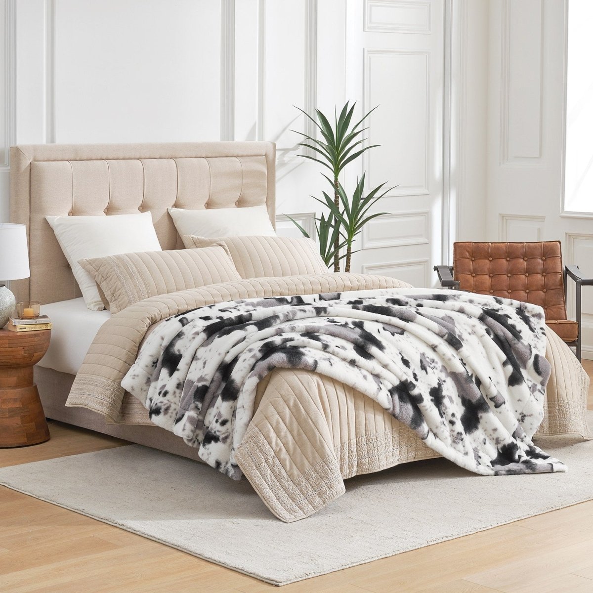 Cow print faux fur throw blanket draped on bed, a cozy and soft luxury blanket for your bedroom. #color_Black/Grey Cow