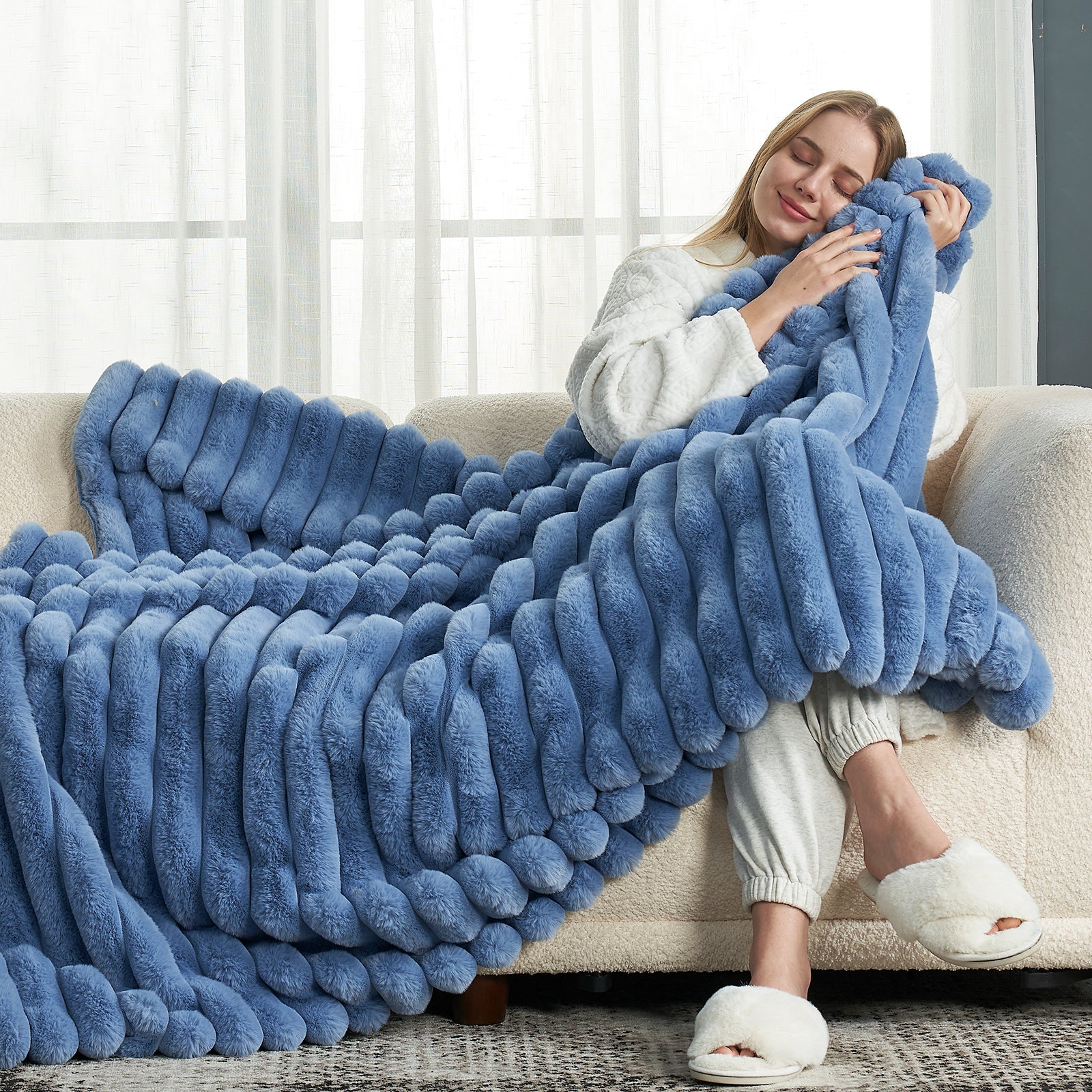 Woman relaxing with blue faux fur Cozy Bliss striped blanket on a sofa. Soft and cozy bedding. #color_Light Blue