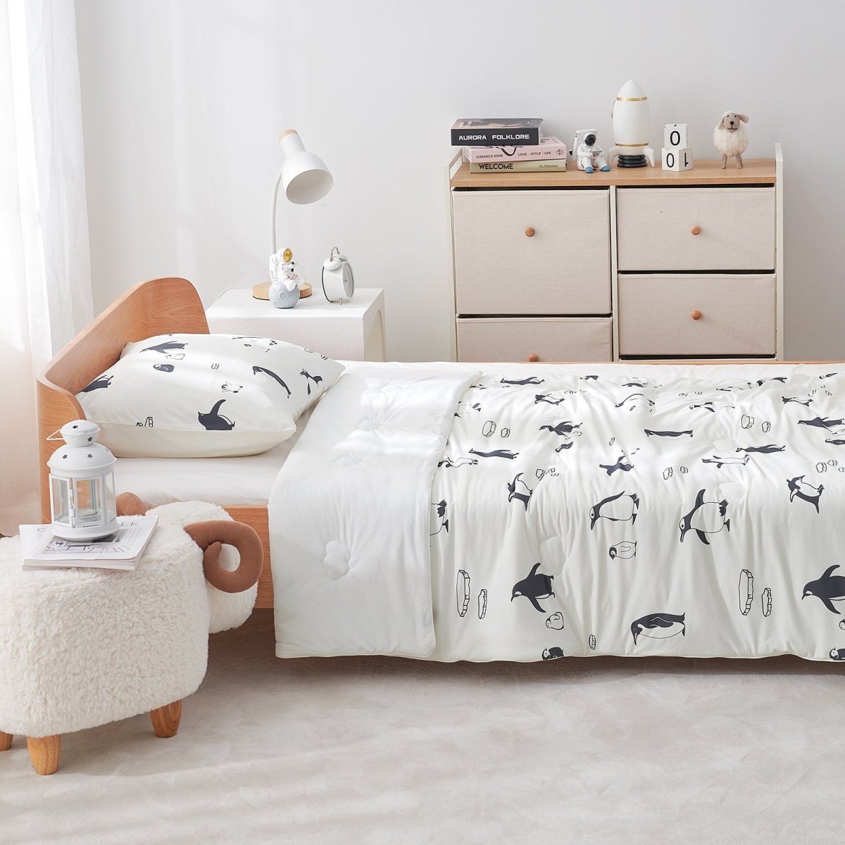 Bedroom with a bed featuring a white comforter with antarctic penguin patterns, wooden headboard, and light-colored furniture.#color_Antarctic Penguin