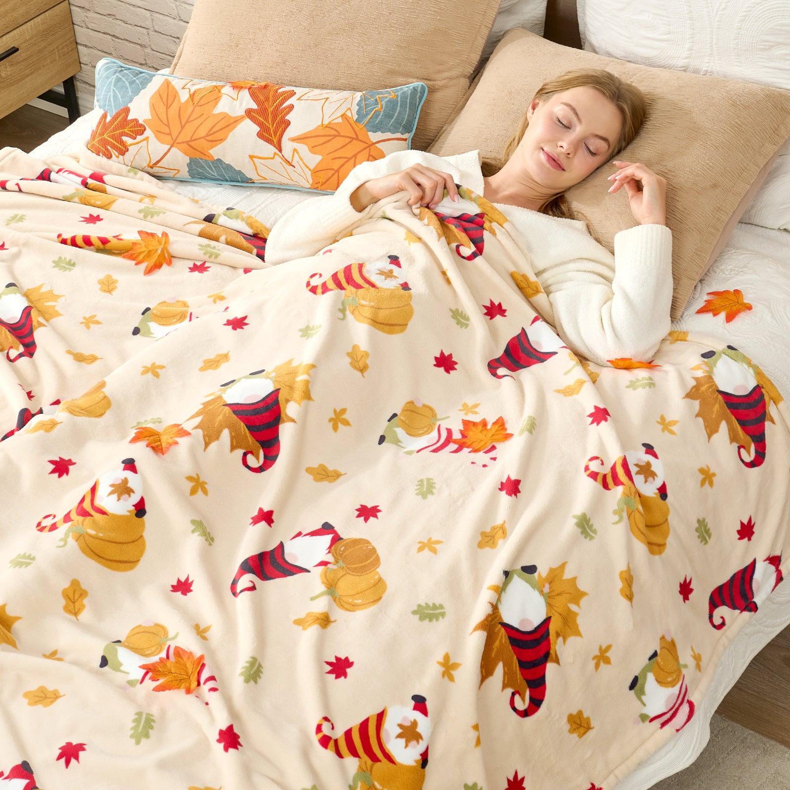 Woman sleeping under a colorful blanket with fall-themed designs on a bed. #color_Pumpkin Gnome