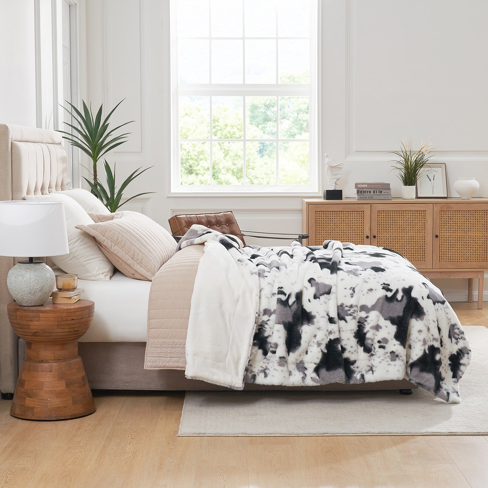 Cow print faux fur throw blanket draped on bed in stylish bedroom setting, cozy bedding #color_Black/Grey