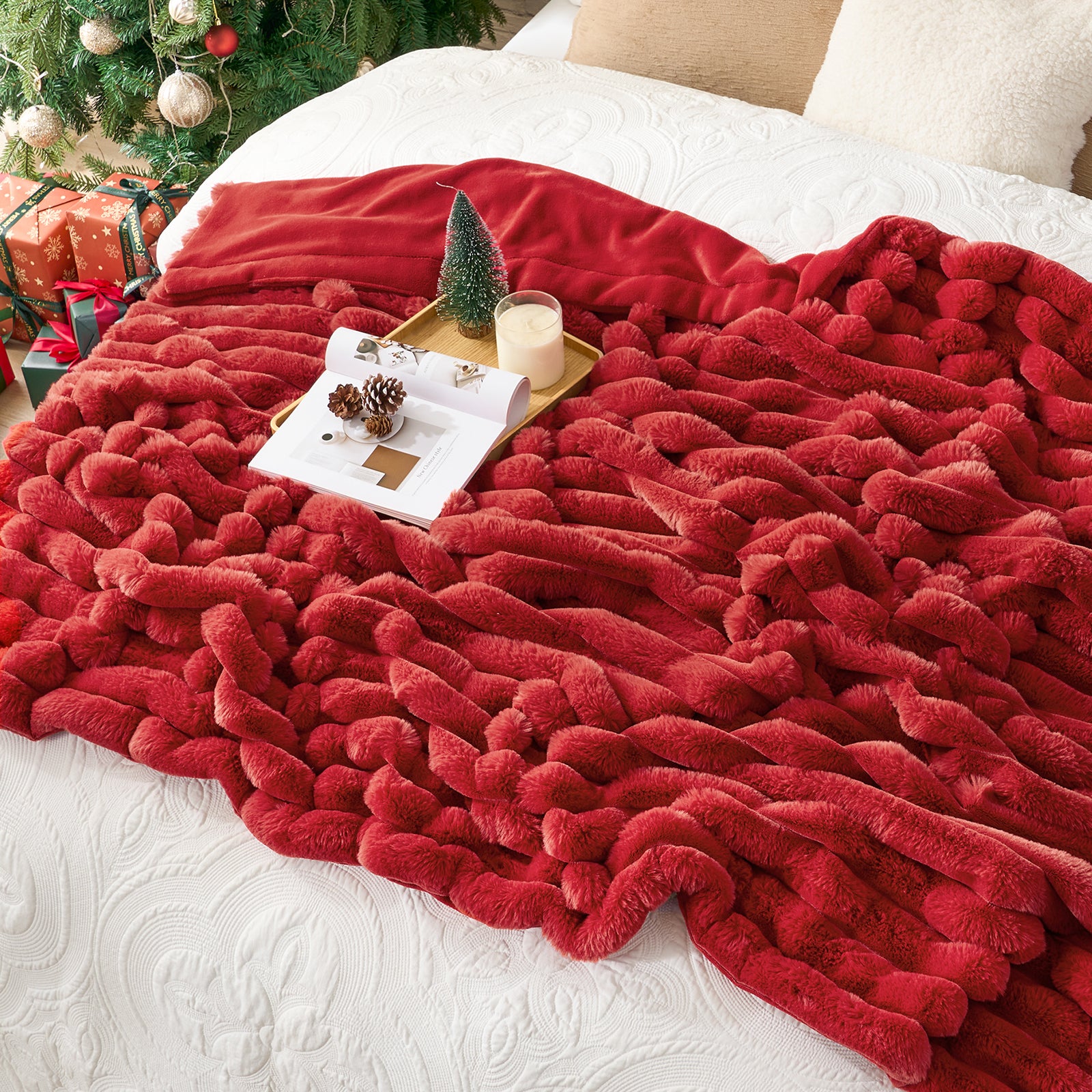Red textured blanket draped over a surface with a Christmas tree and presents in the background. #color_Cardinal Red