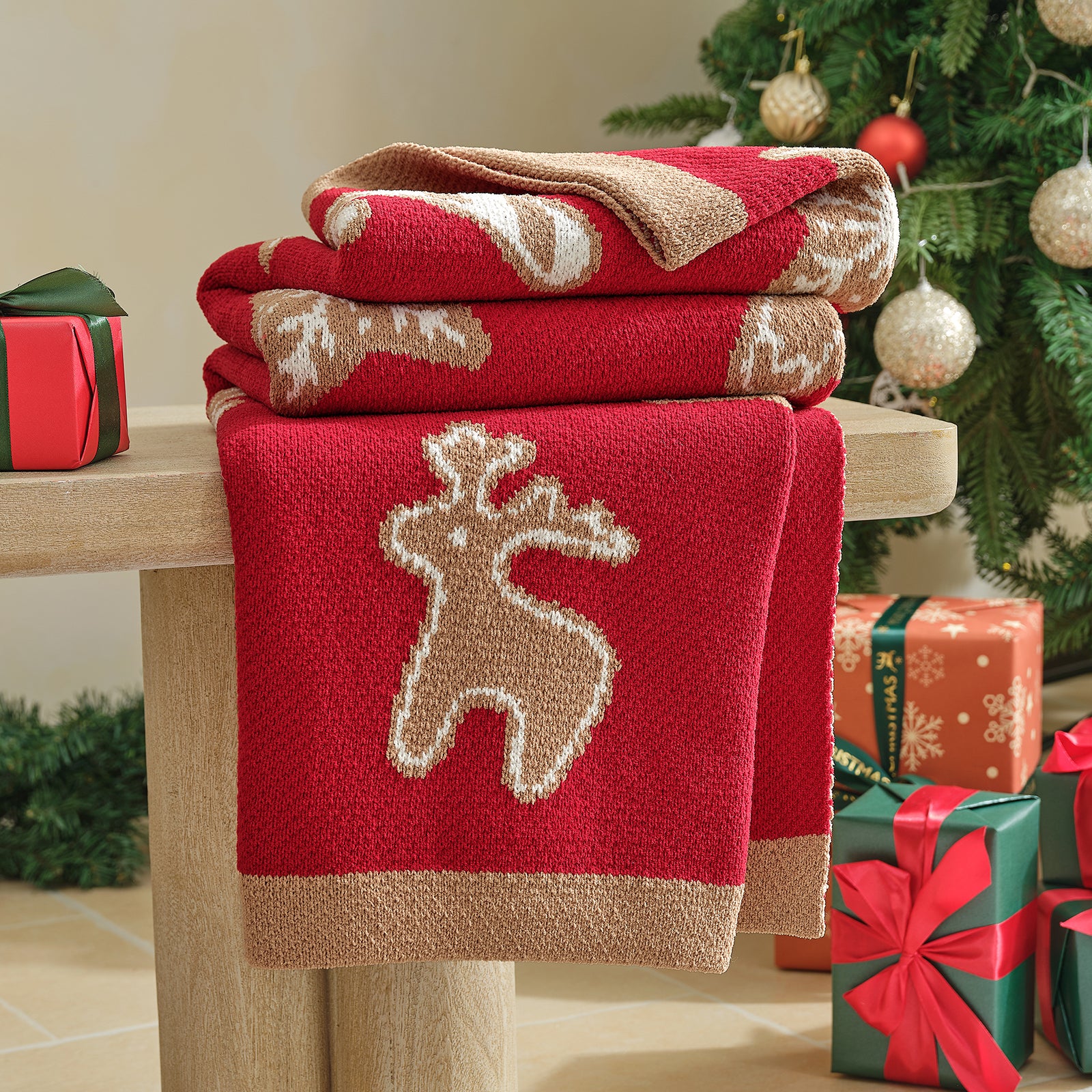 Red and beige towels with a reindeer design on a wooden surface, Christmas tree and gifts in the background. #color_Gingerbread Cookie