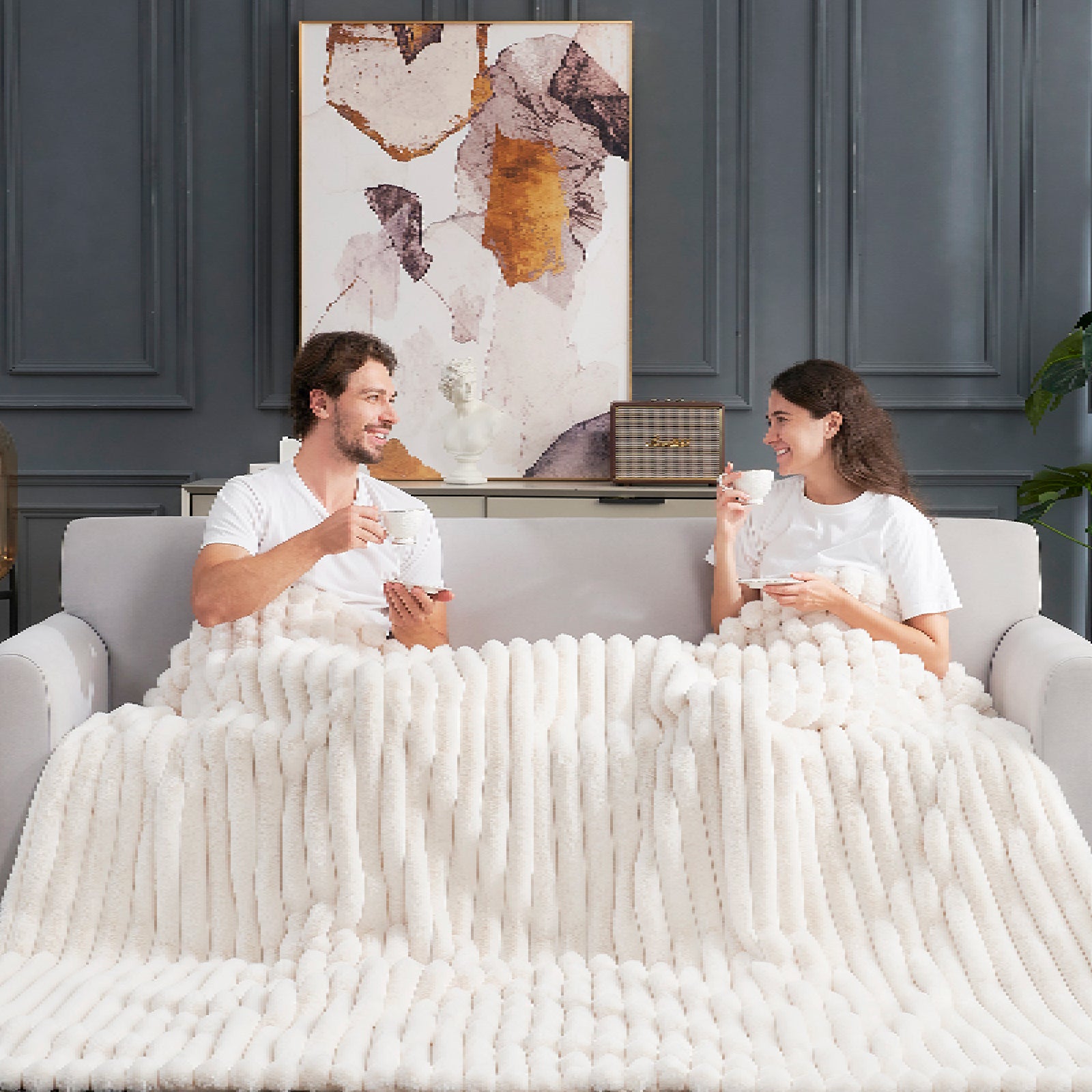 Couple relaxing on sofa with Cozy Bliss faux fur blanket #color_Cream White