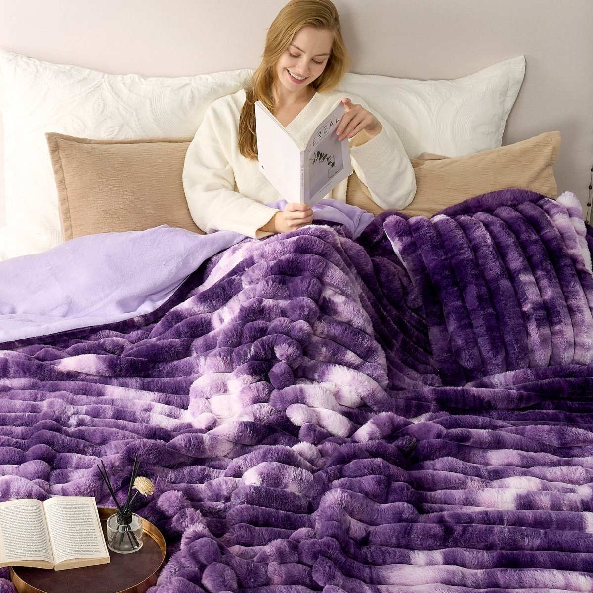 Woman reading a book under a purple blanket on a bed. #color_Tie-dye Purple