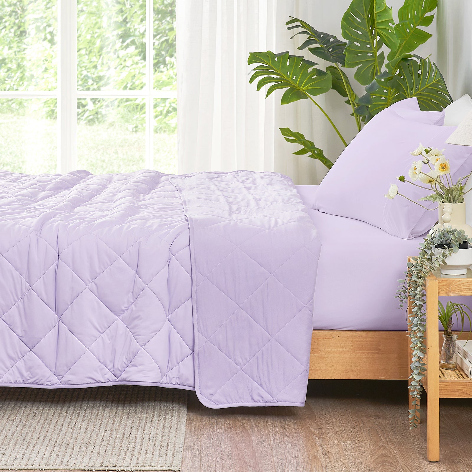 Bed with a purple quilt and pillows in a bright room with plants #color_Purple