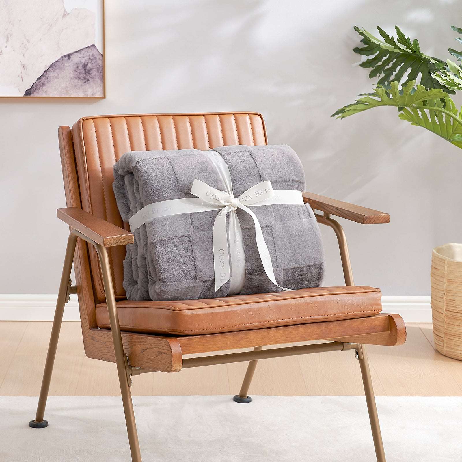 Cozy Bliss gray faux fur blanket, tied with ribbon, on leather chair - perfect for cozy bedding. #color_Grey