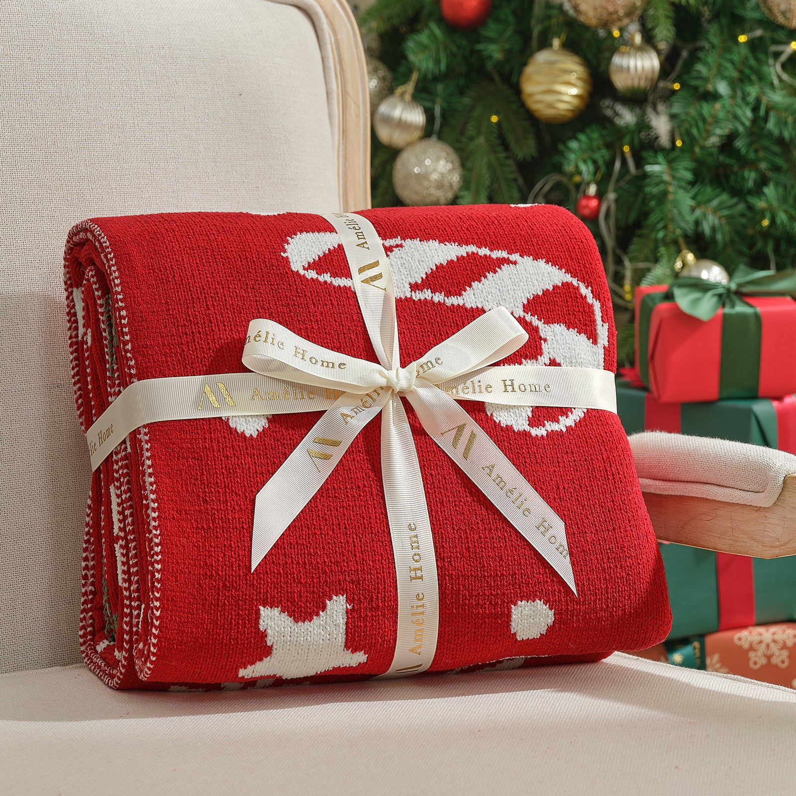 Red blanket with white patterns and a bow, featuring 'Amelie Home' branding, against a festive background with Christmas tree and presents. #color_Candy Cane
