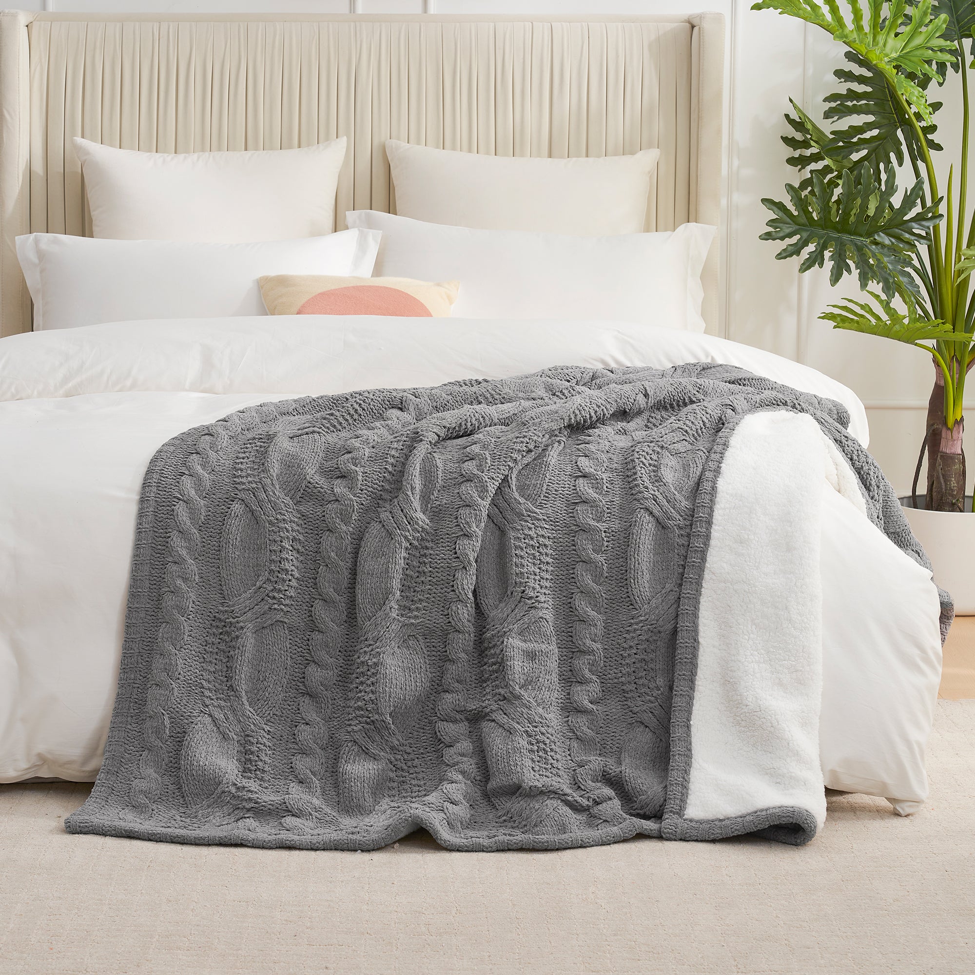Gray cable knit blanket on a bed with white bedding and pillows, in a room with a plant. #Color_Grey