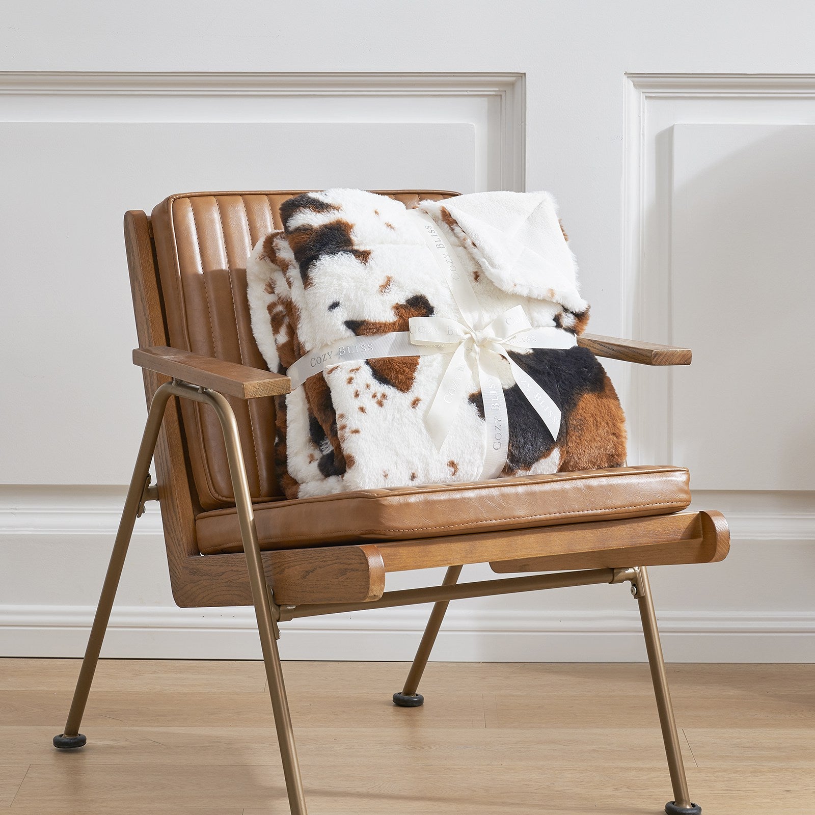 Cow print faux fur throw blanket on brown chair. Featuring Cozy Bliss ribbon. Cozy bedding #color_Black/Brown