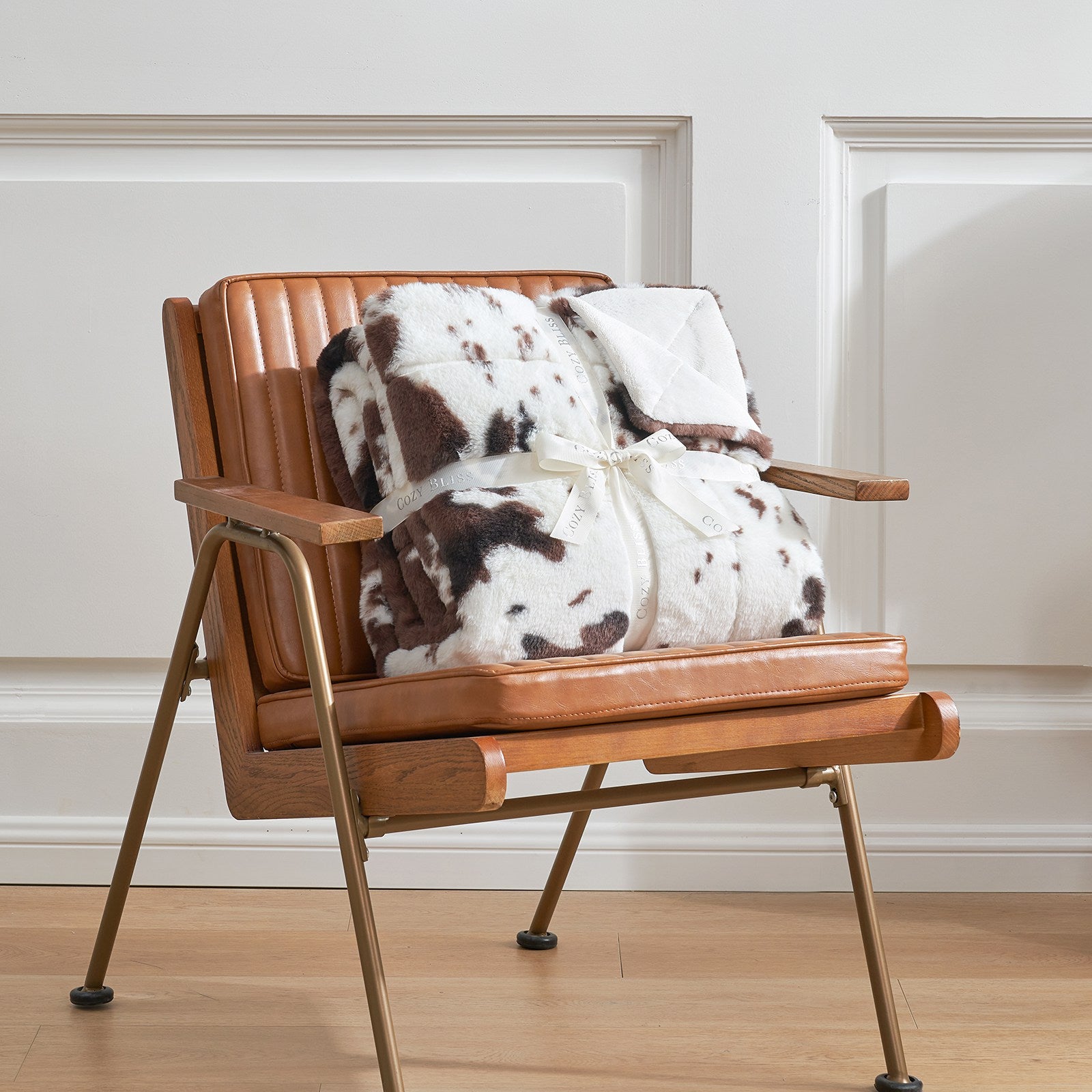COZY BLISS cow print faux fur blanket draped on brown leather chair, cozy bedding #color_Black/Coffee