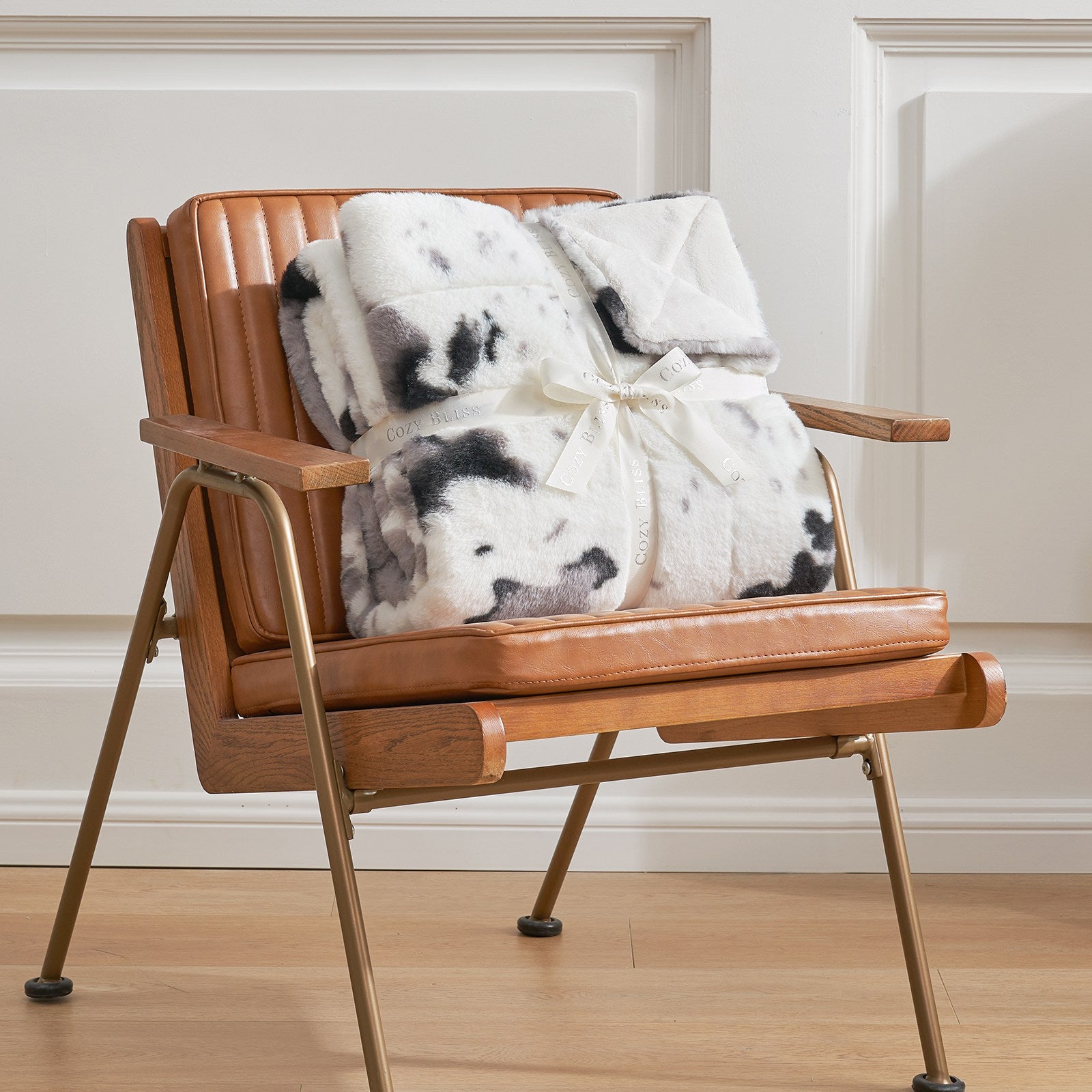 Cow print faux fur blanket on brown leather chair, a cozy bedding from COZY BLISS #color_Black/Grey