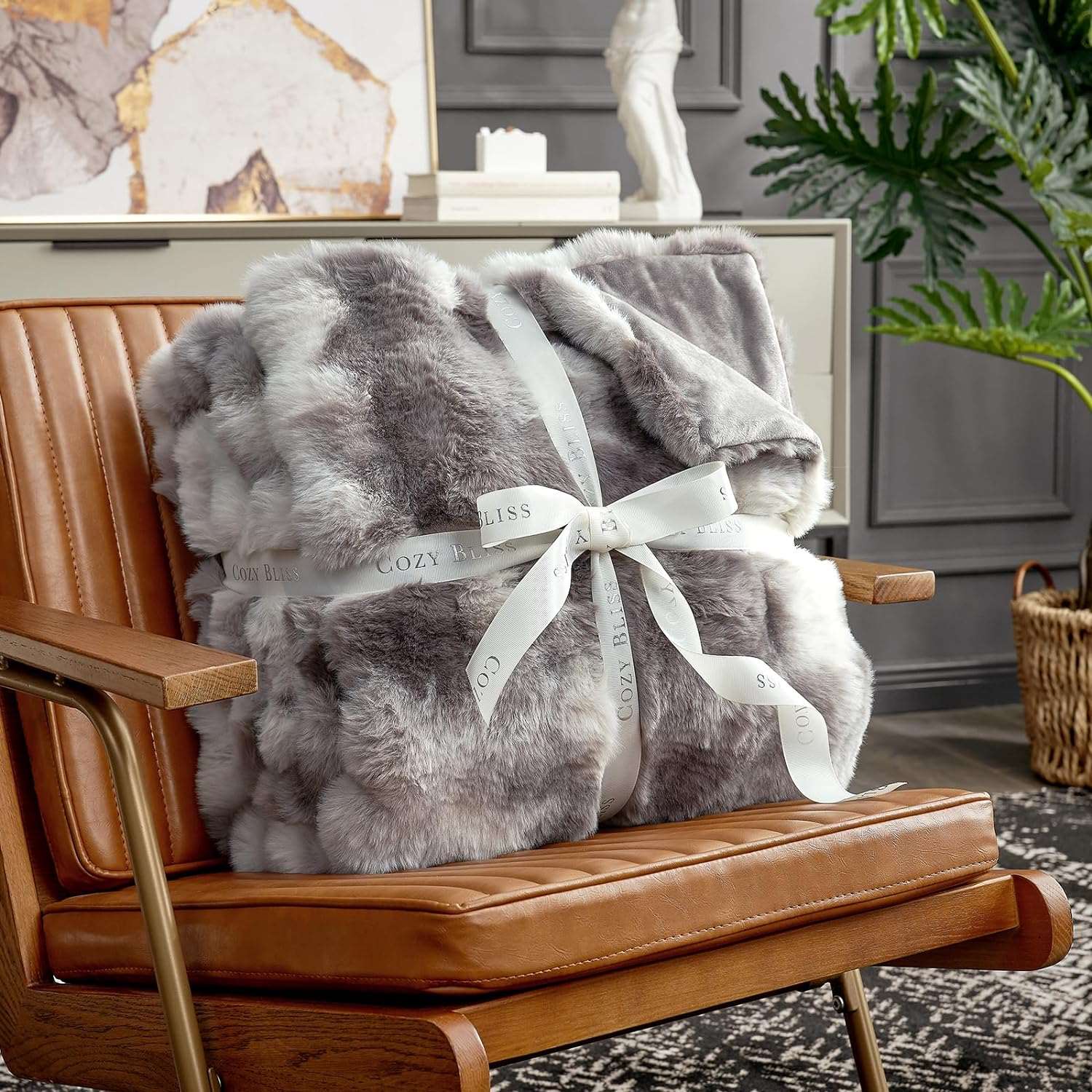 Cozy Bliss tie-dye taupe faux fur throw blanket, tied with ribbon, on a brown chair. #color_Tie-dye Taupe