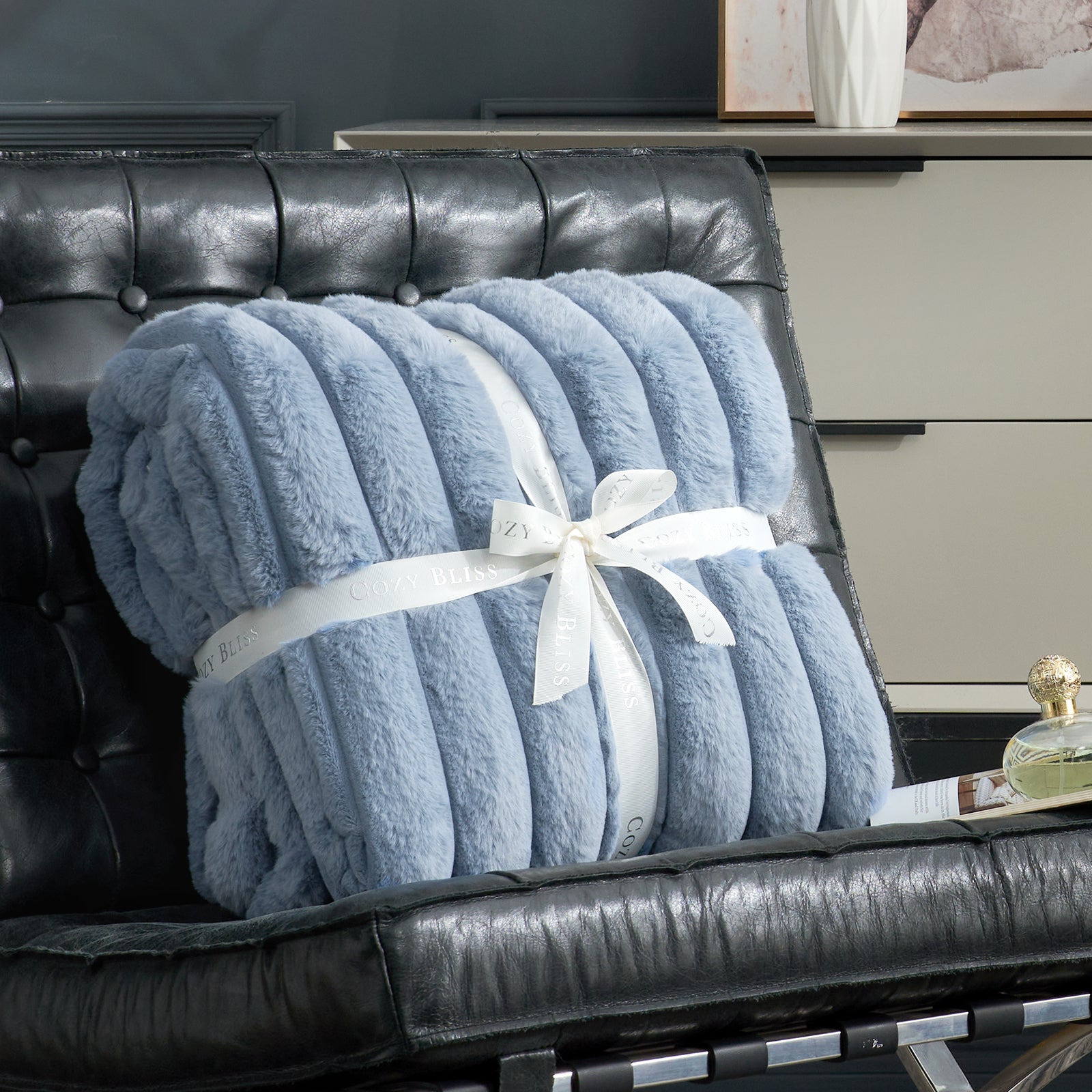 Blue blanket with a white ribbon on a black leather chair. #color_Blue