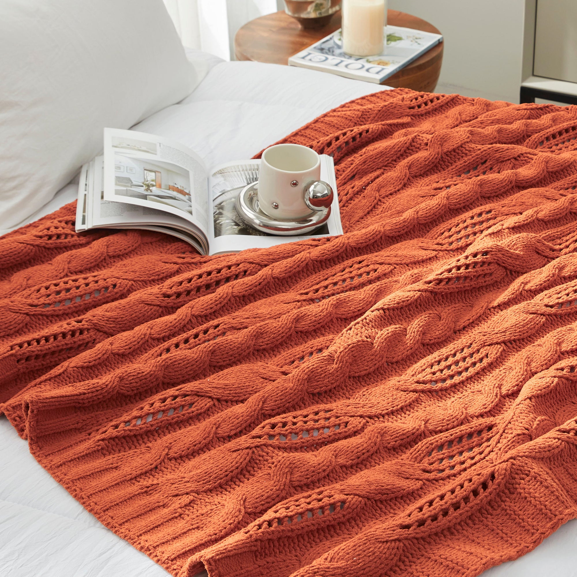 Chenille Cable Knit Throw Blanket in Burnt Orange styled on a bed, adding warmth and a vibrant cozy touch. #color_Burnt Orange