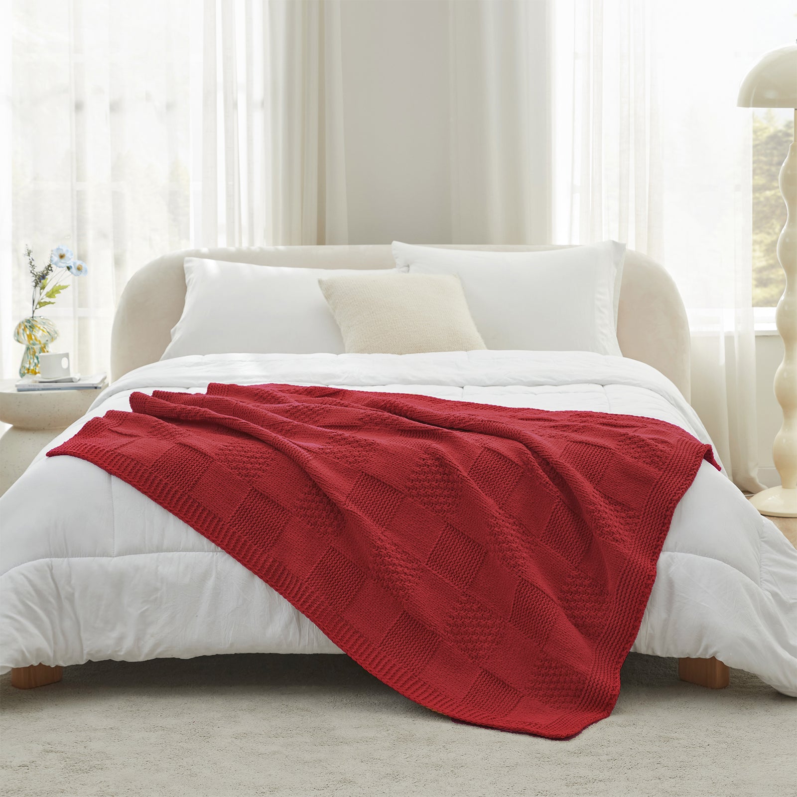 Red blanket on a bed in a bright bedroom with white bedding and curtains. #color_Christmas Red