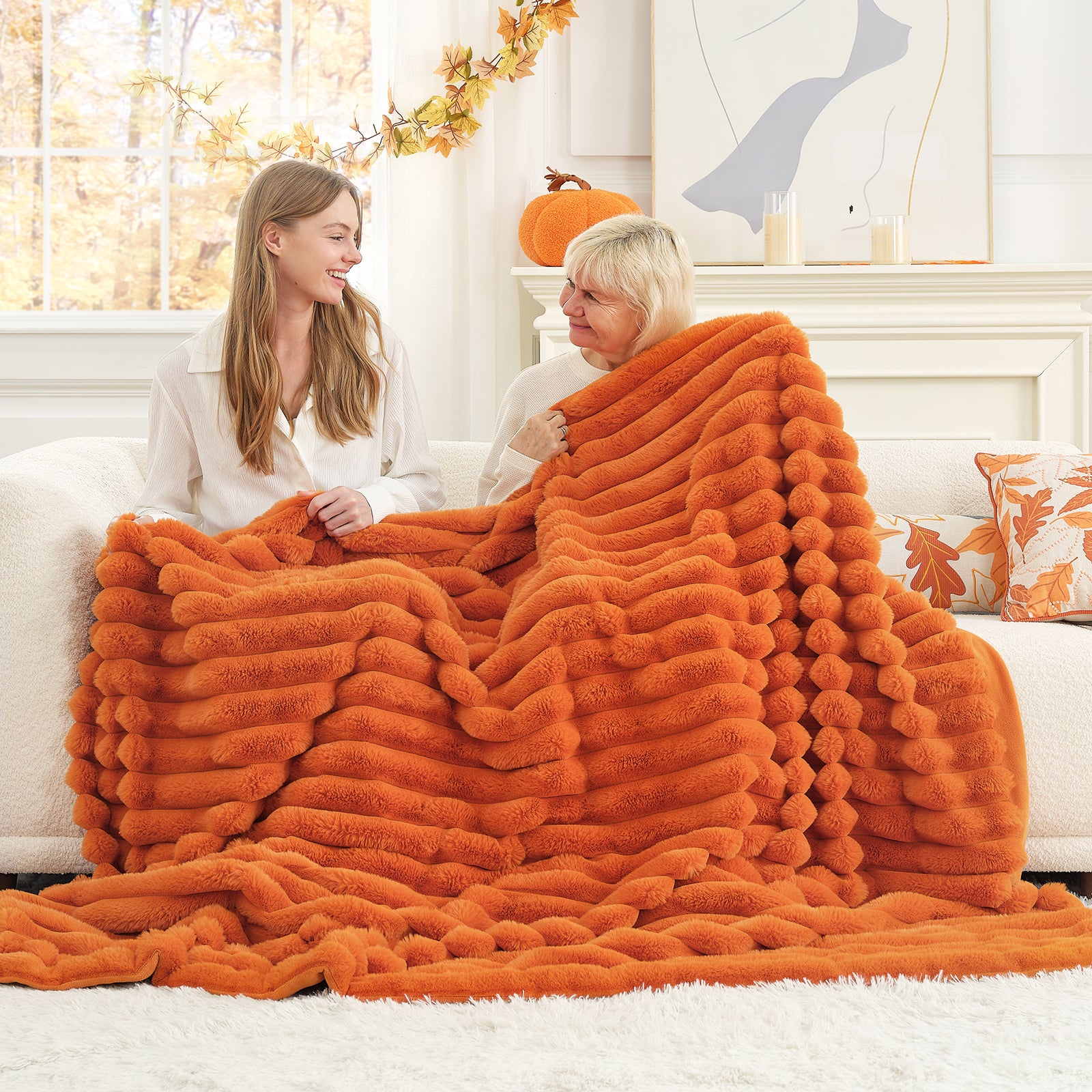Two women sitting on a couch under an orange fluffy blanket in a cozy living room. #color_Burnt Orange