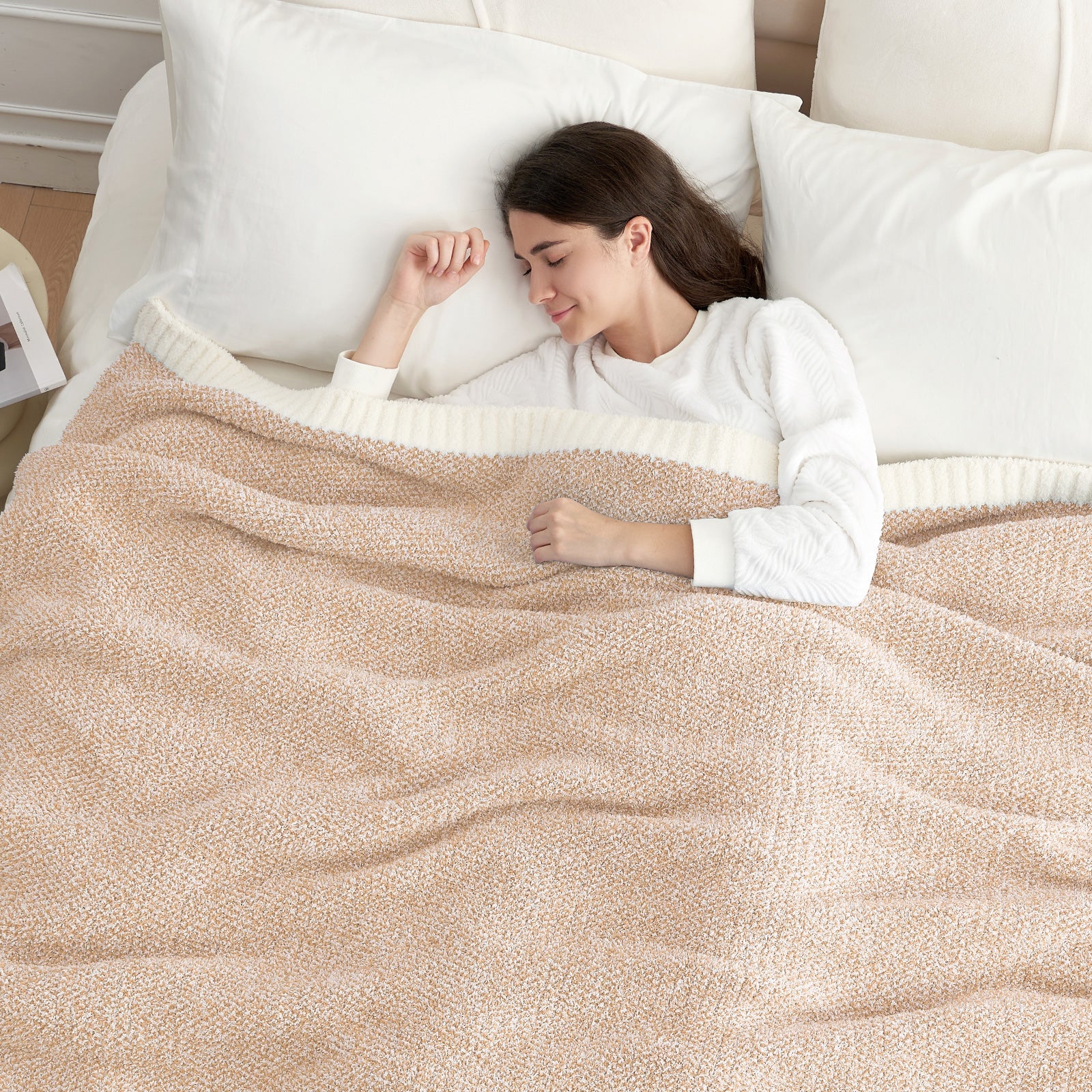 Woman lying on a bed with a Heather Feather Yarn Throw Blanket in Beige, ideal for rest. #color_Beige