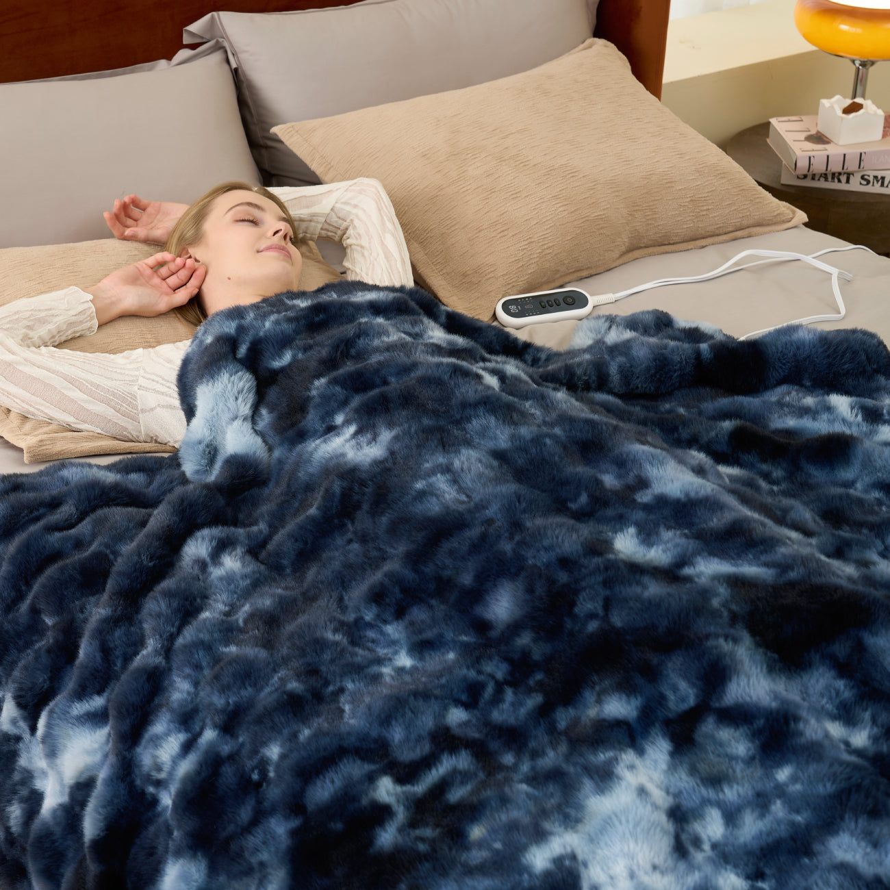 Woman lying in bed under a blue blanket with a remote control on the nightstand. #color_Tie-dye Blue