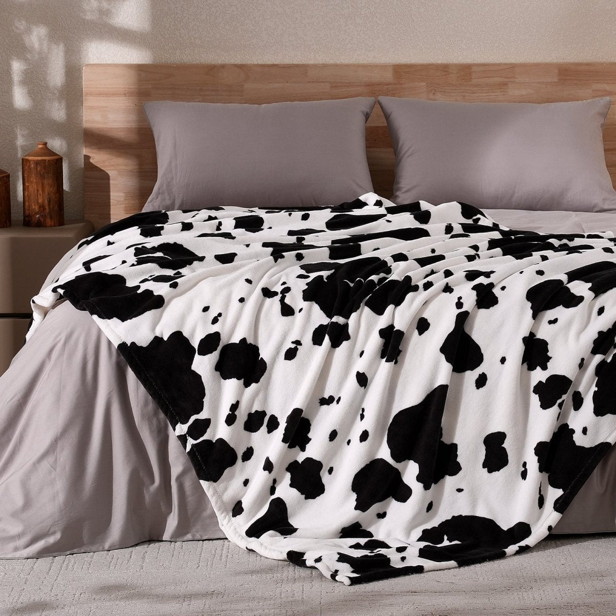 Cow print milkyplush throw blanket in Black & White draped over a bed, creating a stylish atmosphere #color_Black & White