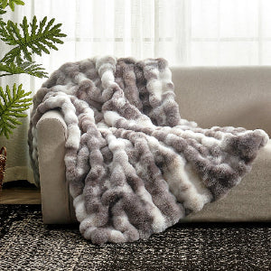 Fluffy gray and white blanket draped over a sofa with a plant in the background