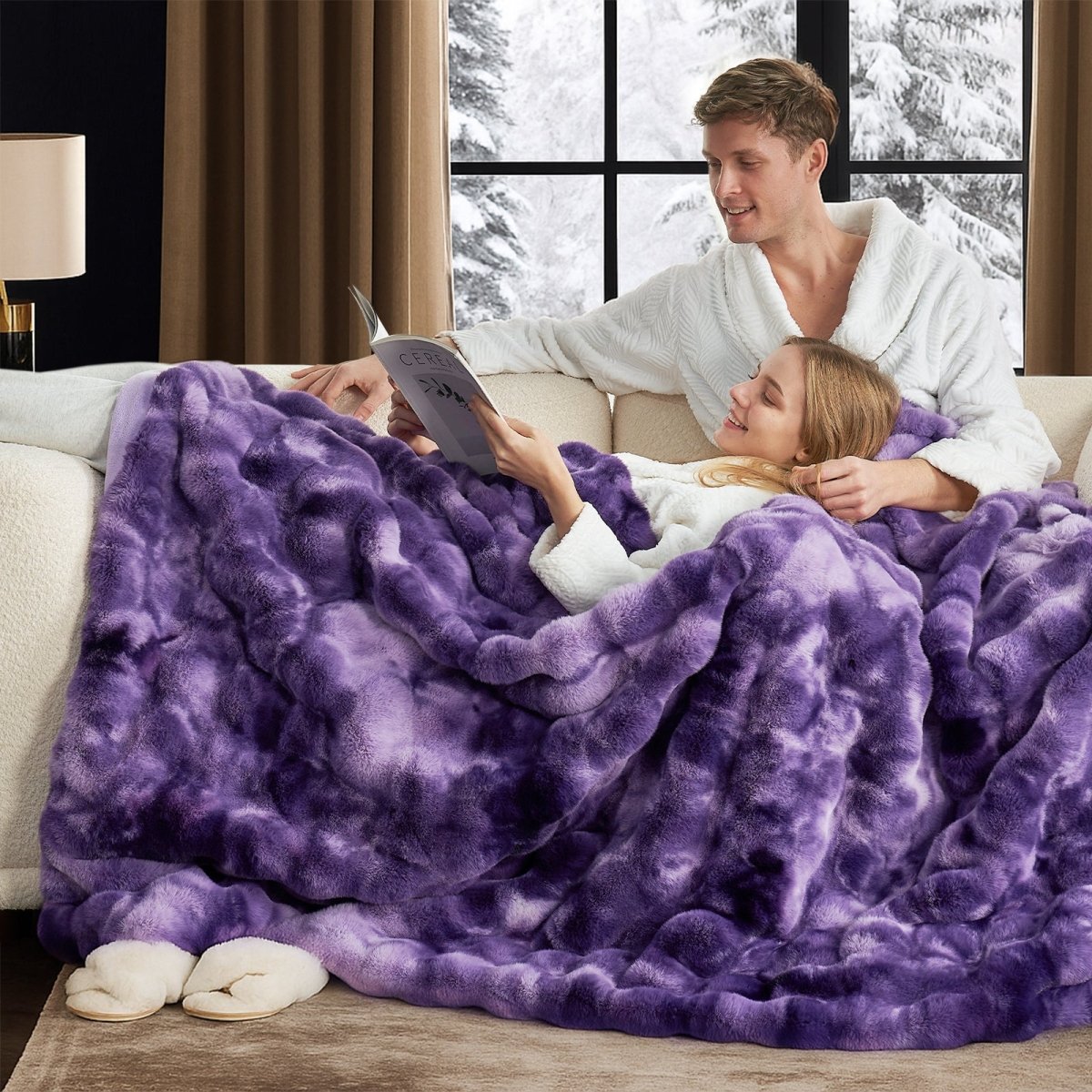 Man and woman under a purple blanket on a couch with a snowy window view. #color_Tie-dye Purple