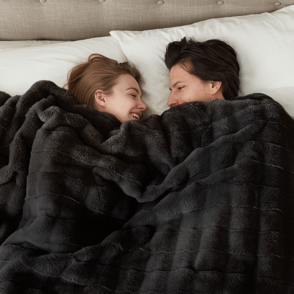 Couple relaxing under a cross-striped faux fur throw blanket on a sofa. #Color_Black