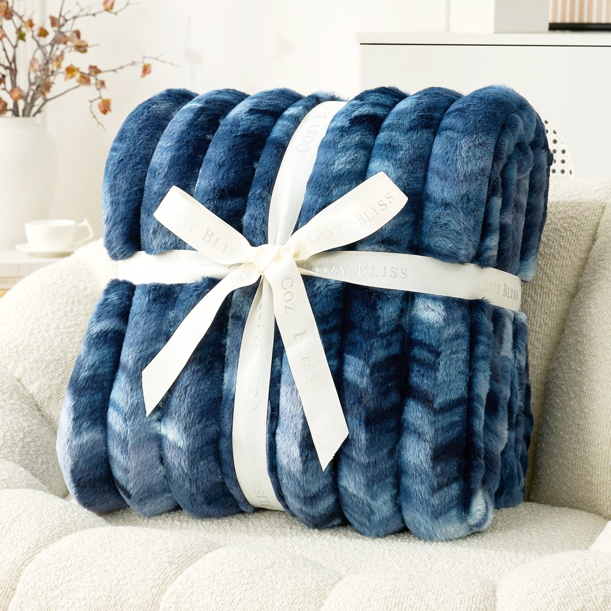 Blue textured blanket with a white ribbon on a light-colored couch. #color_Tie-dye Blue