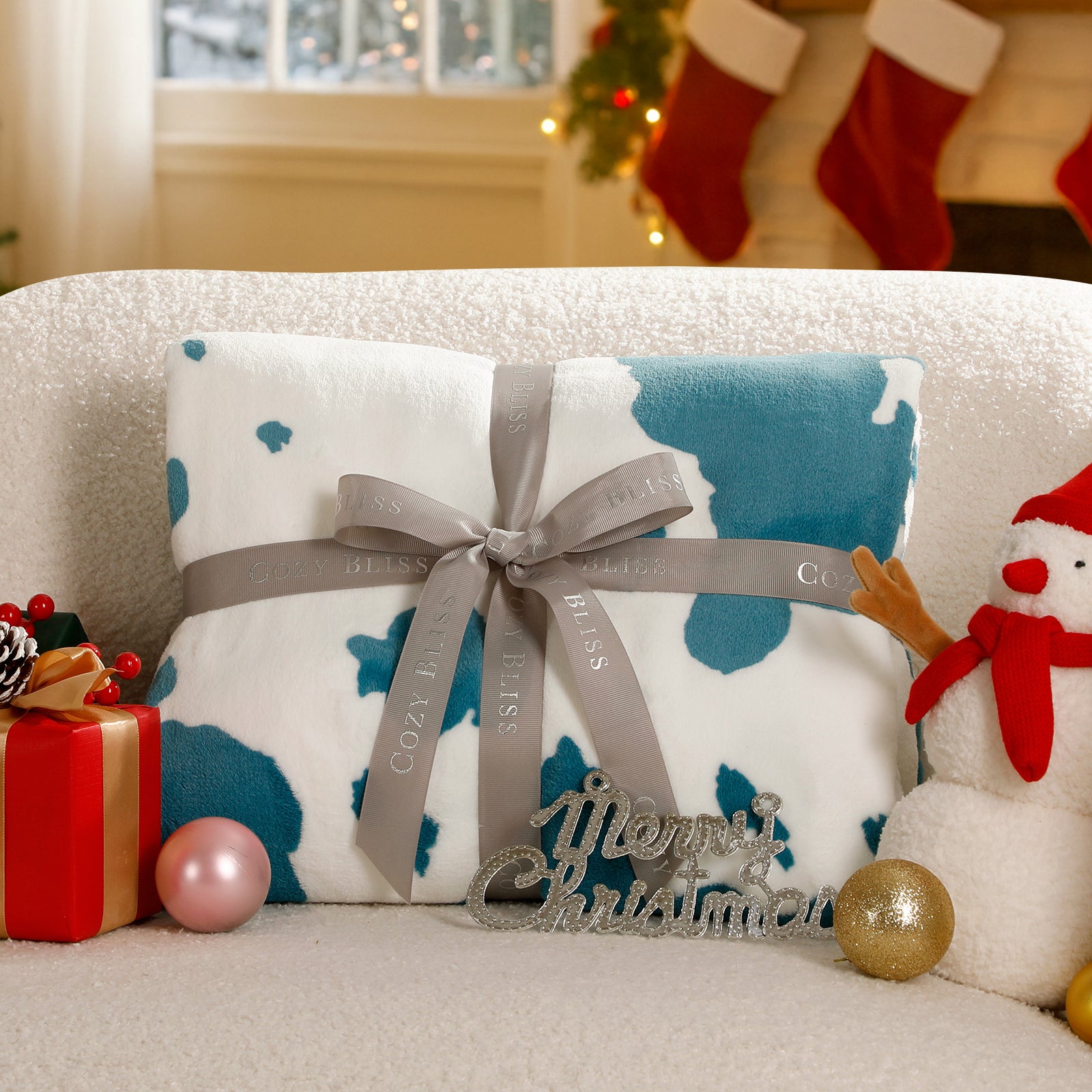 Christmas-themed gift with decorative bow and 'Merry Christmas' ornament on a couch. #color_Blue