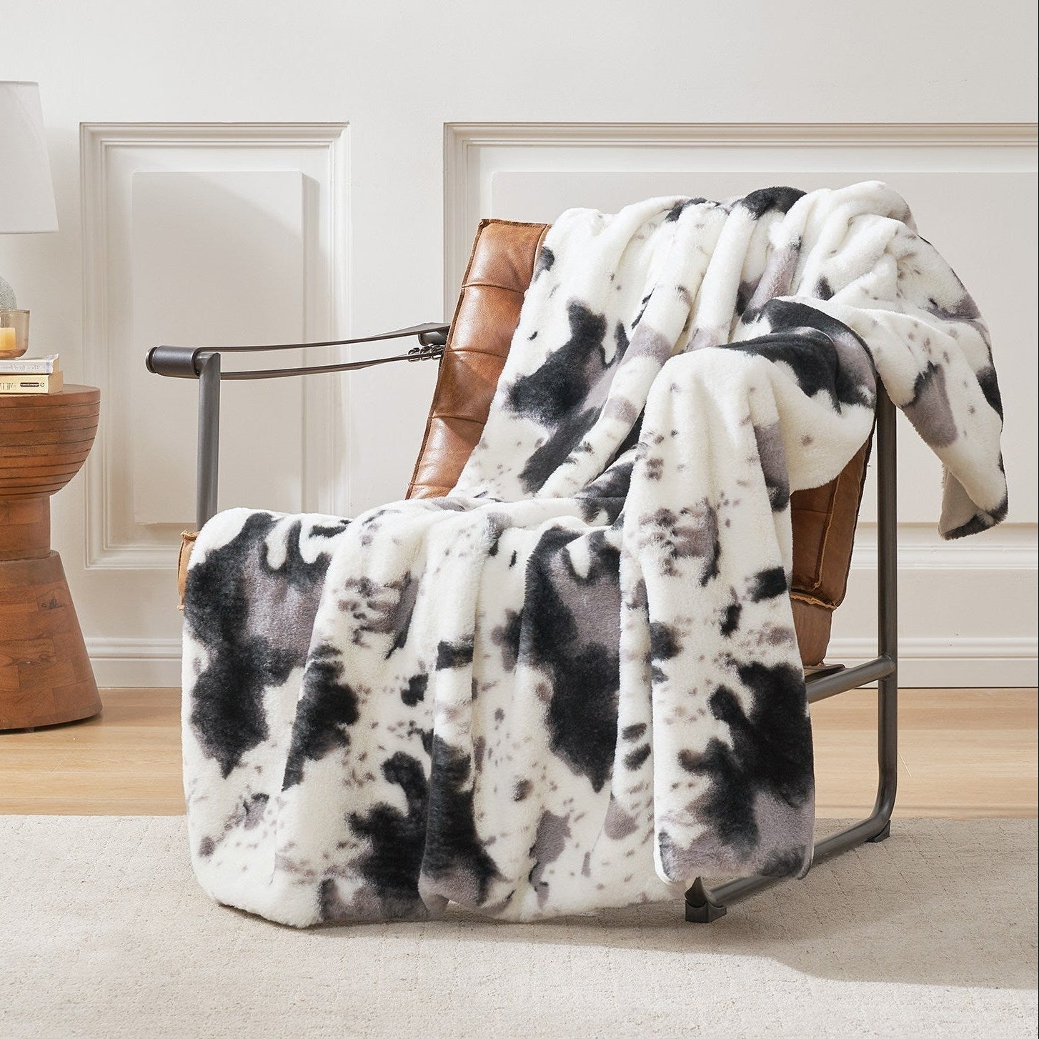 Cow print faux fur throw blanket draped over a chair, cozy bedding #color_Black/Grey Cow