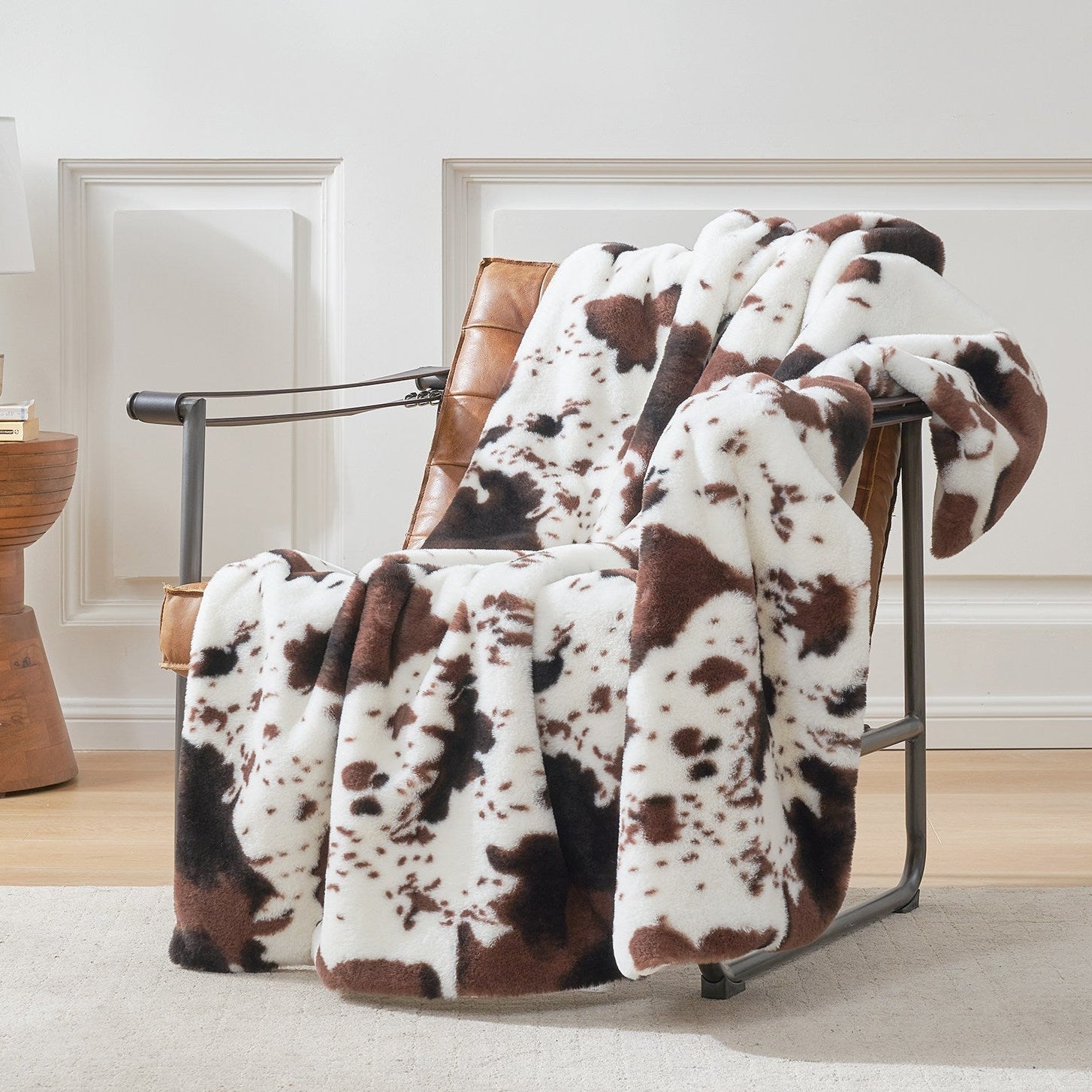 Cow print faux fur blanket draped over leather chair. Soft, cozy cow print blanket for home decor. #color_Black/Coffee