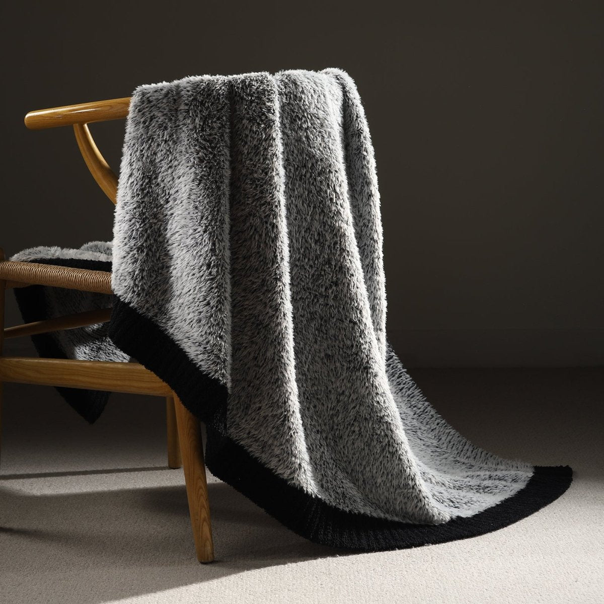 Faux Mink Feather Knit Throw Blanket in Black draped over a chair, showcasing soft faux mink texture and elegant knit design. #color_Black