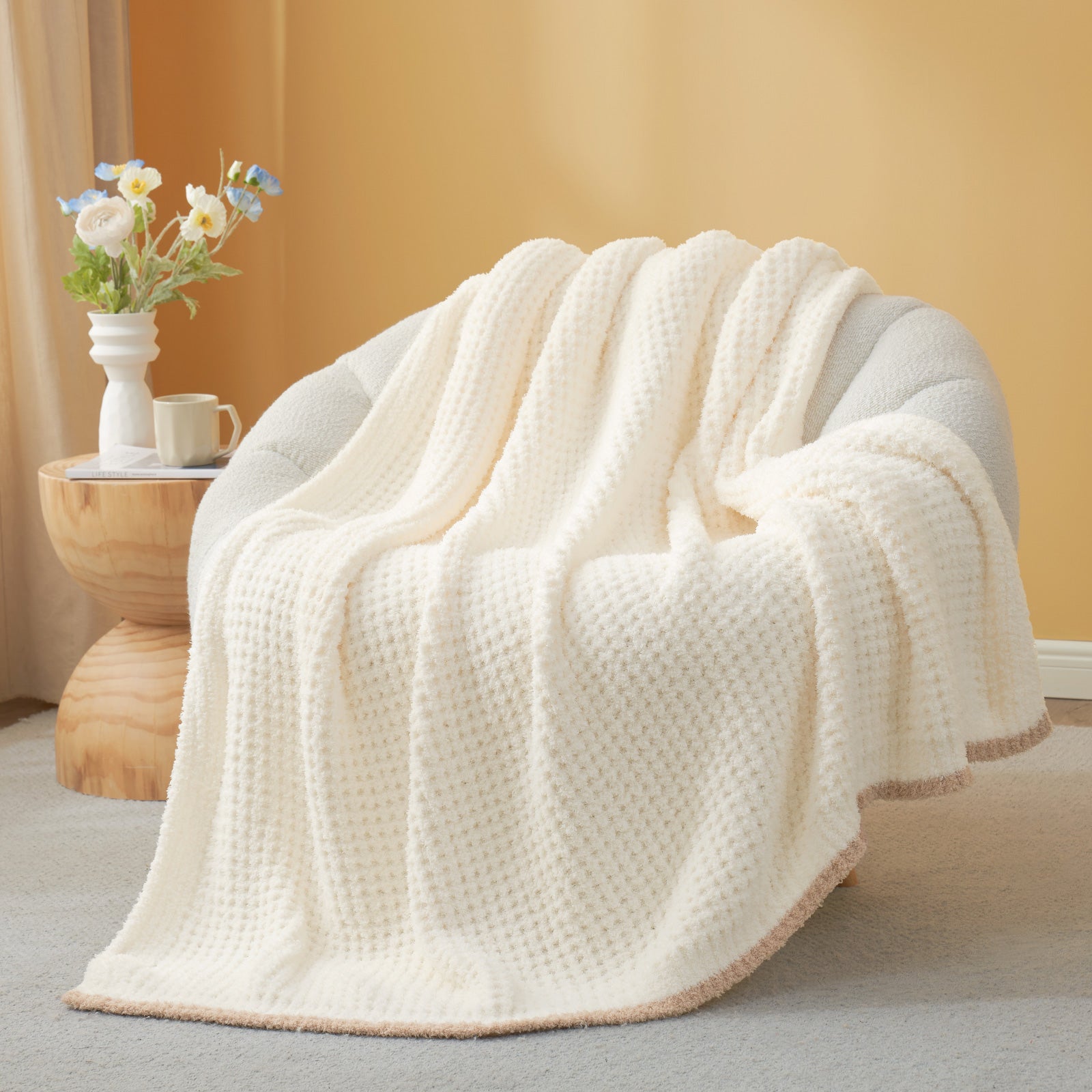 White textured blanket draped over a chair with a side table and flowers in the background. #color_Cream White