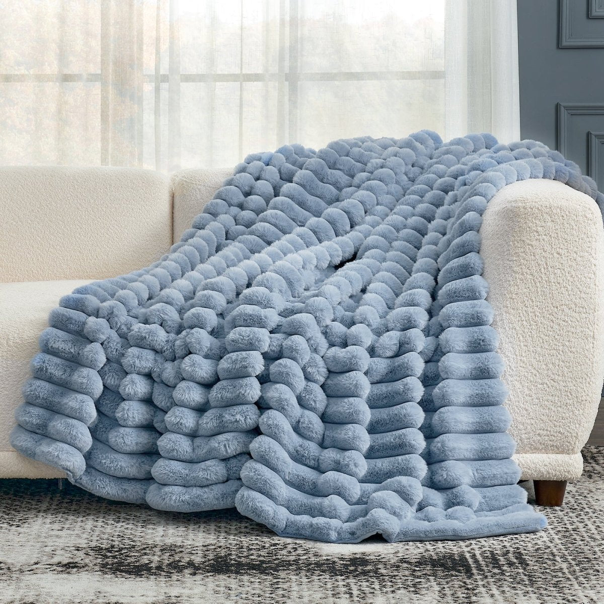 Cozy Bliss blue striped faux fur throw blanket draped over a white couch in a living room setting. #color_Misty Blue