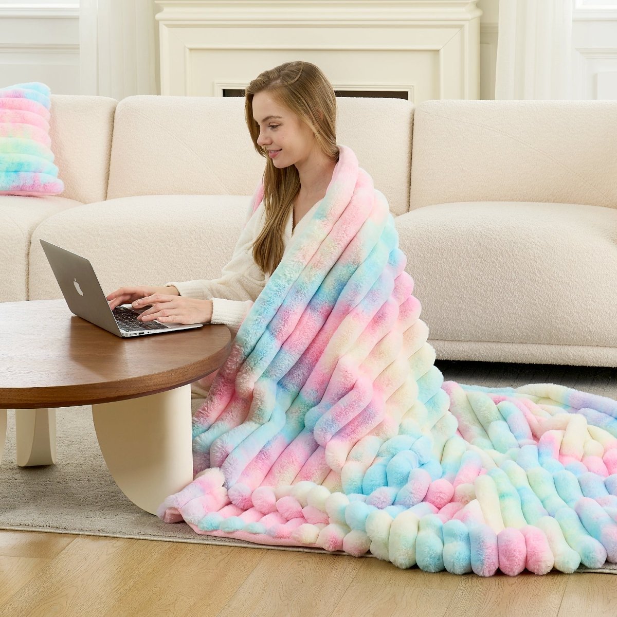 Woman sitting on the floor with a colorful blanket, using a laptop in a cozy living room. #color_Tie-dye Rainbow