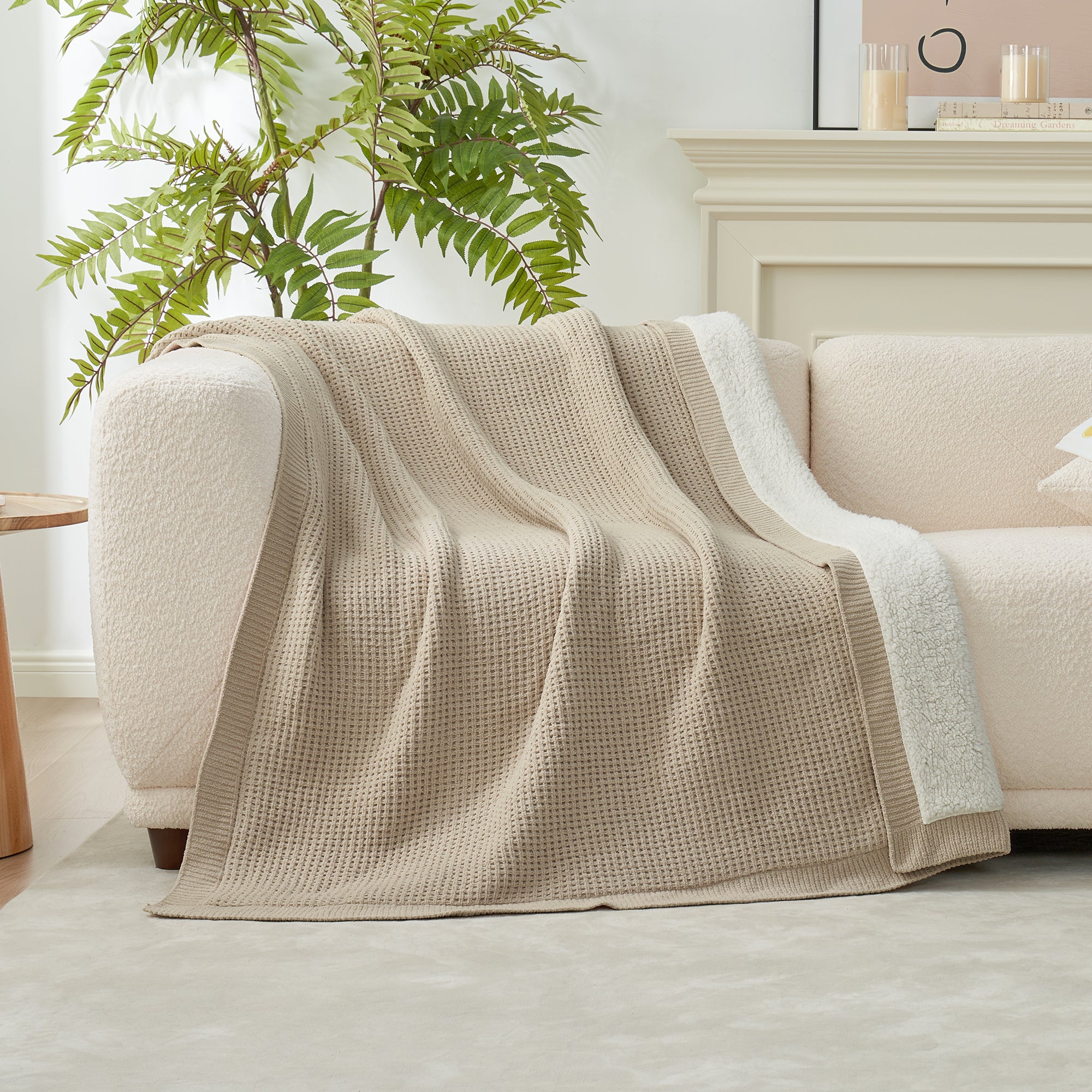 Beige blanket draped over a beige sofa in a living room with a plant and candles in the background. #color_Beige