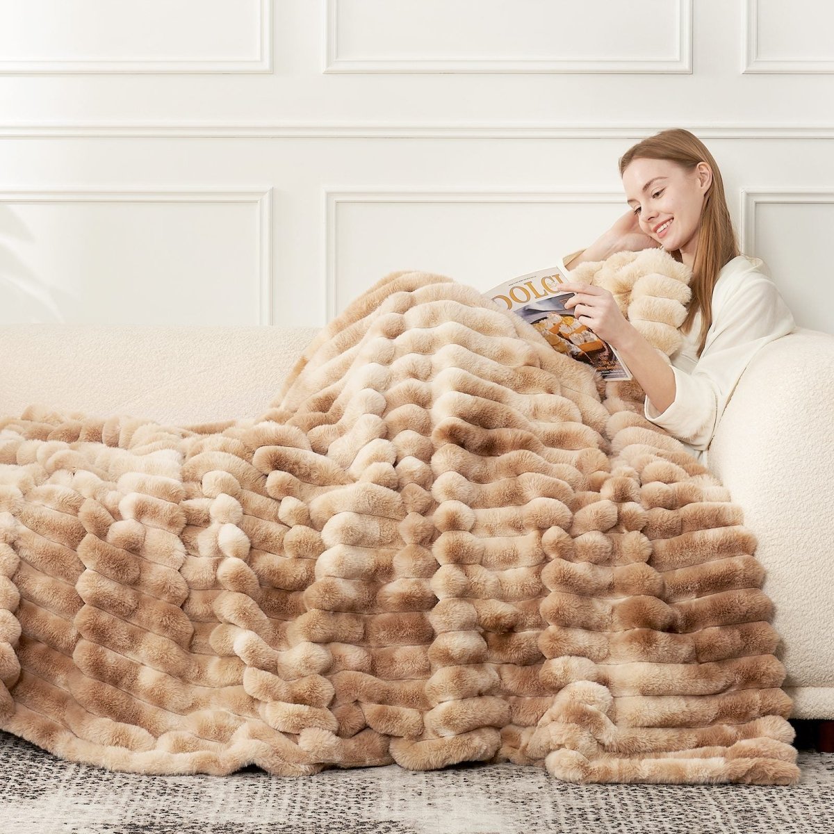 Woman reading on a couch wearing Striped faux fur blanket in tie-dye beige. #color_Tie-dye Beige
