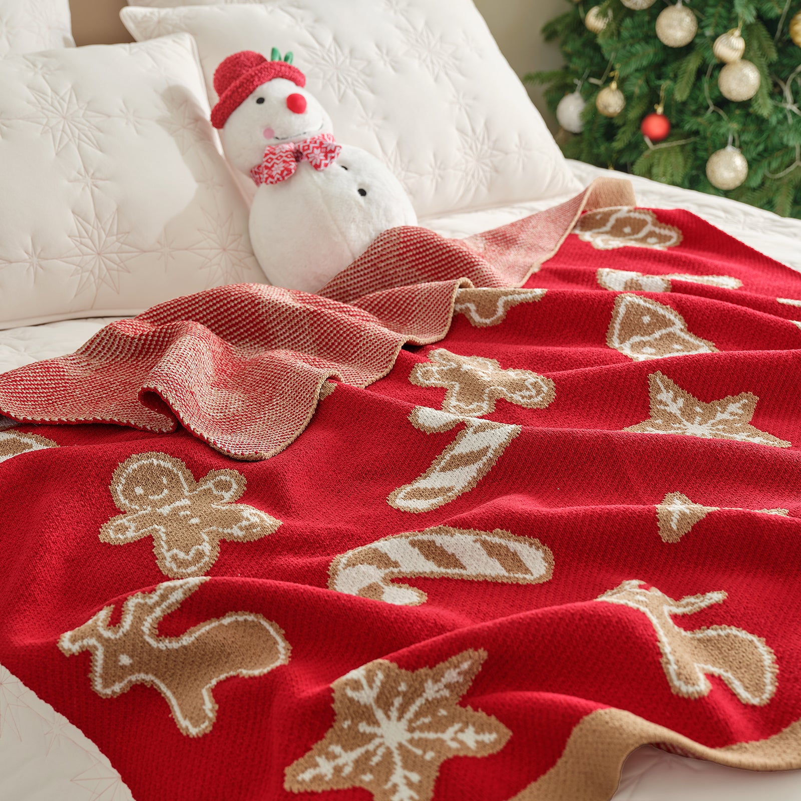 Red Christmas-themed blanket with gingerbread men, snowflakes, and candy canes on a bed with a snowman plush toy. #color_Gingerbread Cookie