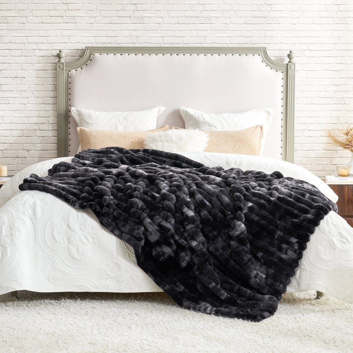 Black faux fur throw blanket on a bed with white bedding and pillows against a brick wall. #color_Tie-dye Black