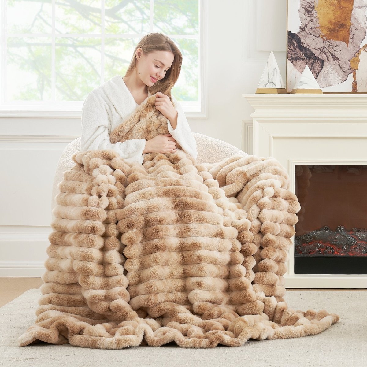 Woman sitting on a sofa wearing Cozy Bliss faux fur blanket in beige stripes. Soft, cozy blanket for comfortable sleep and relaxation. #color_Tie-dye Beige