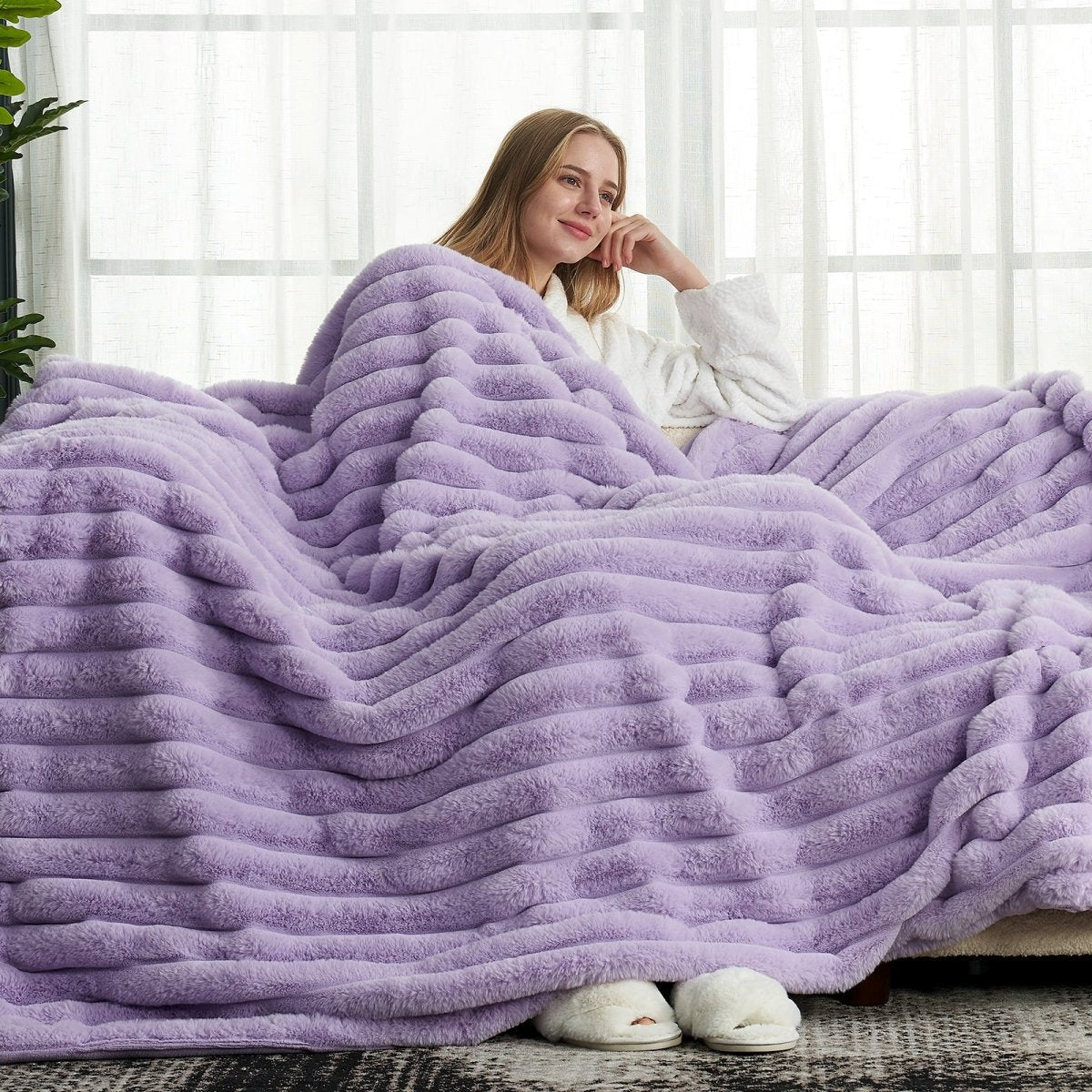 Woman relaxing on a couch with Cozy Bliss purple striped faux fur blanket. #color_Purple