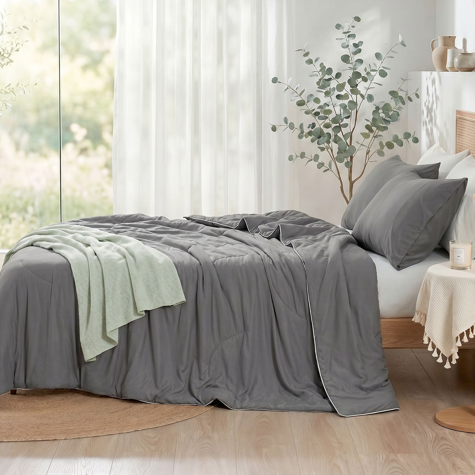 Cozy Bliss double-sided cooling comforter on a bed in a bright, sunlit bedroom with green plants, lightweight summer bedding for hot sleepers.#color_Dark Grey