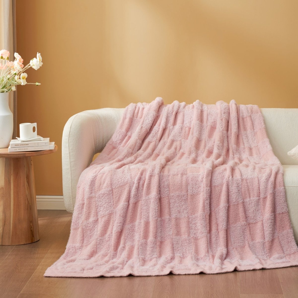 Checkered Faux Fur Feather Yarn Throw Blanket in Pink draped over a sofa, highlighting its gentle tone and texture. #color_Pink