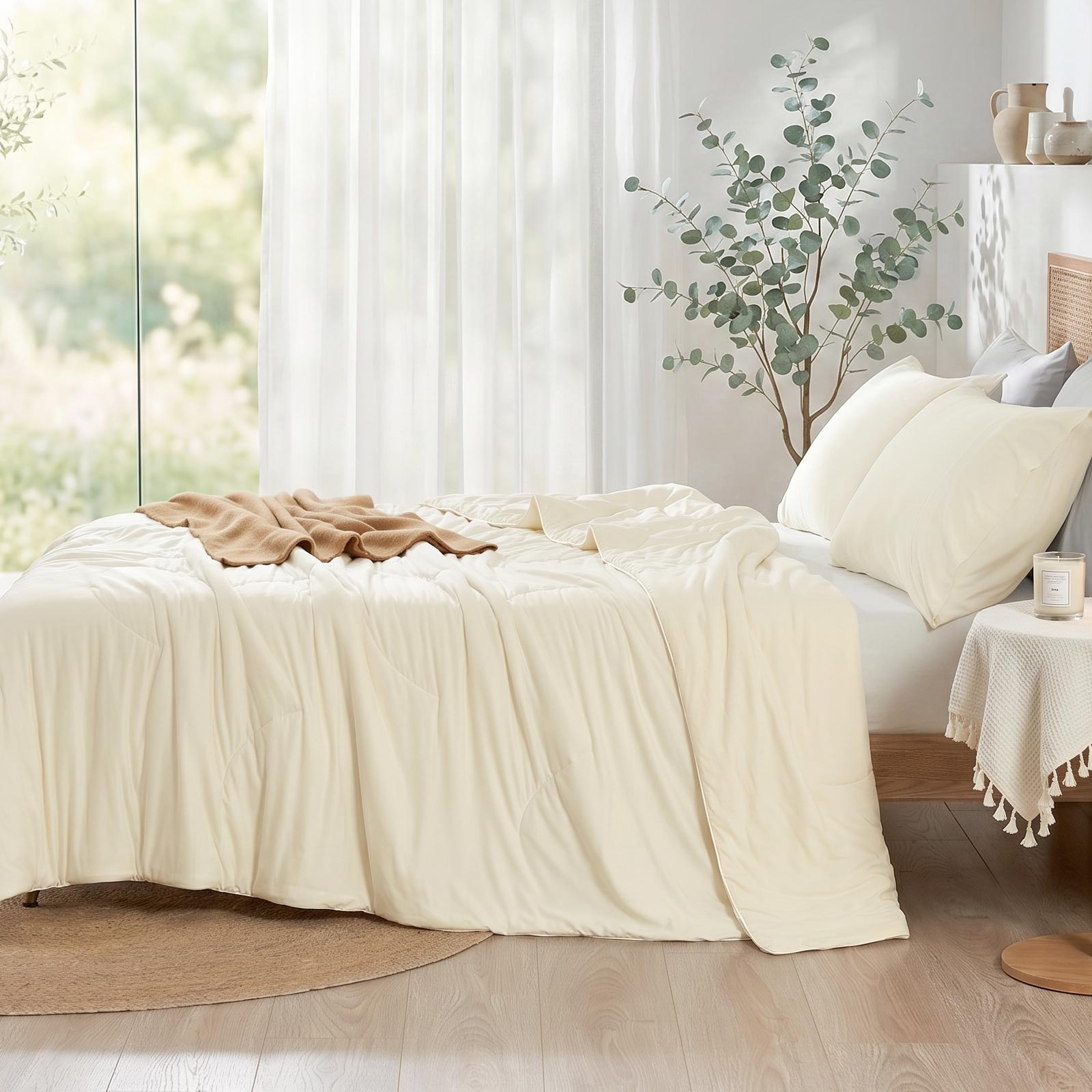Cozy Bliss double-sided cooling comforter on a bed in a bright, sunlit bedroom with green plants, lightweight summer bedding for hot sleepers.#color_Ivory