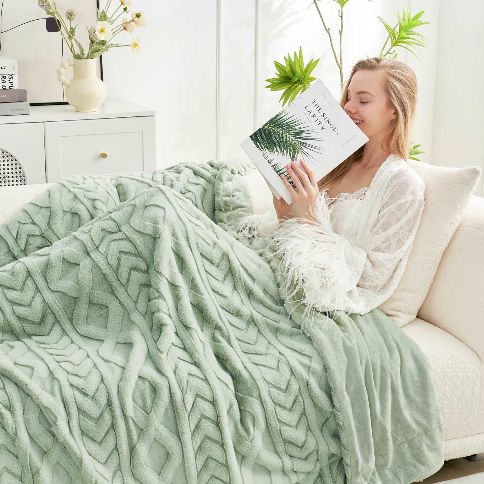 Woman relaxing on sofa with Cozy Bliss cable knit blanket #color_Sage Green