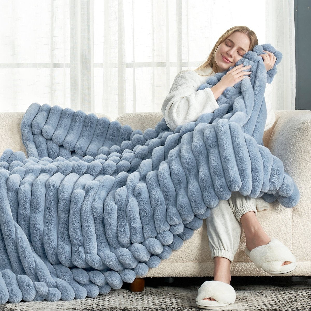 Woman relaxing on sofa with Cozy Bliss blue striped faux fur blanket #color_Misty Blue