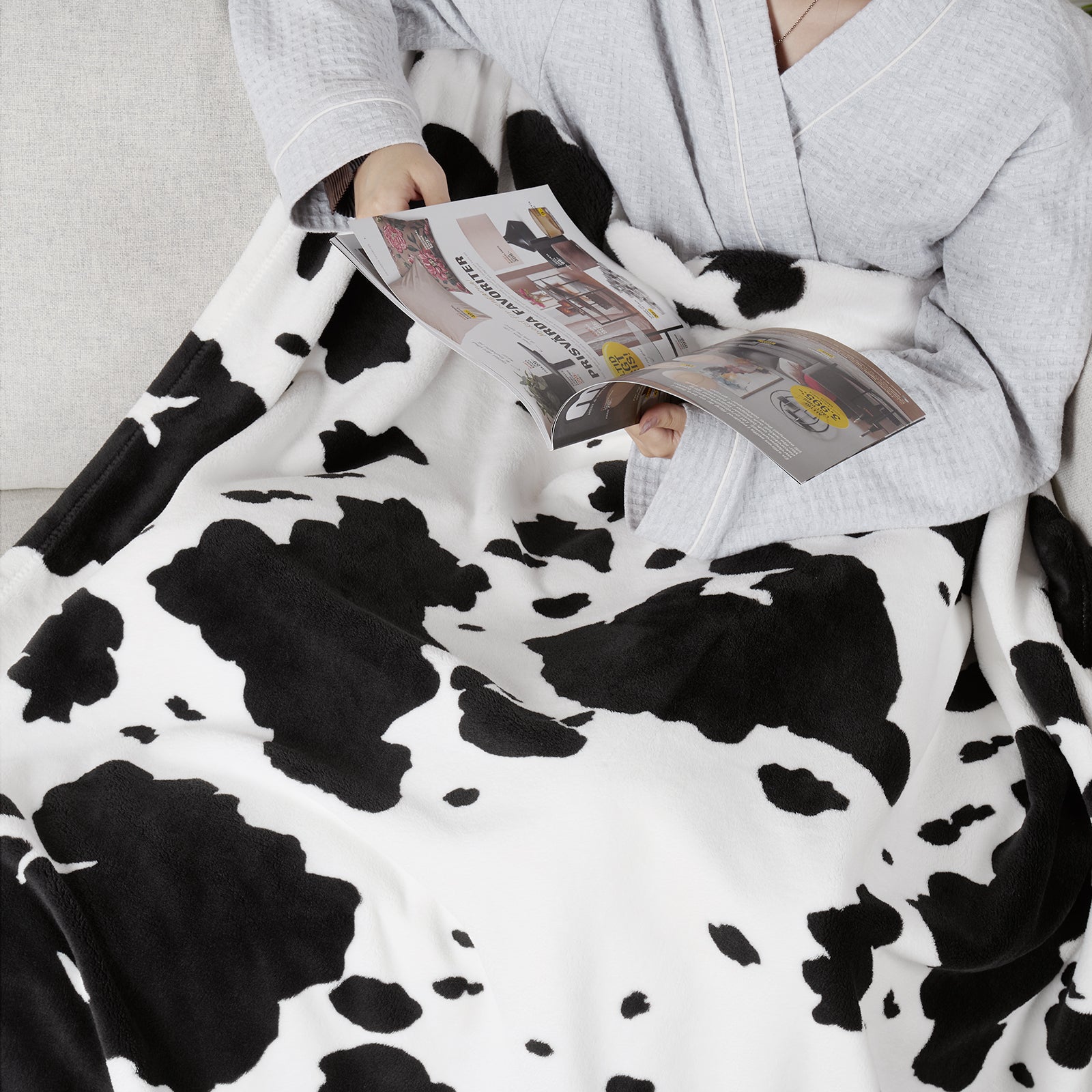 Person reading a newspaper under a cow print blanket #color_Black White