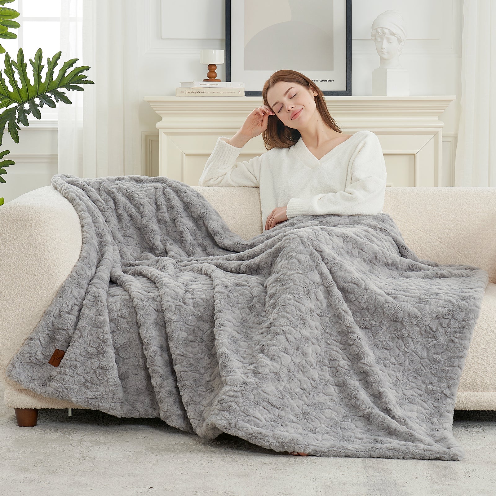 Woman relaxing on a couch under a gray quilt in a cozy living room.  #color_Grey